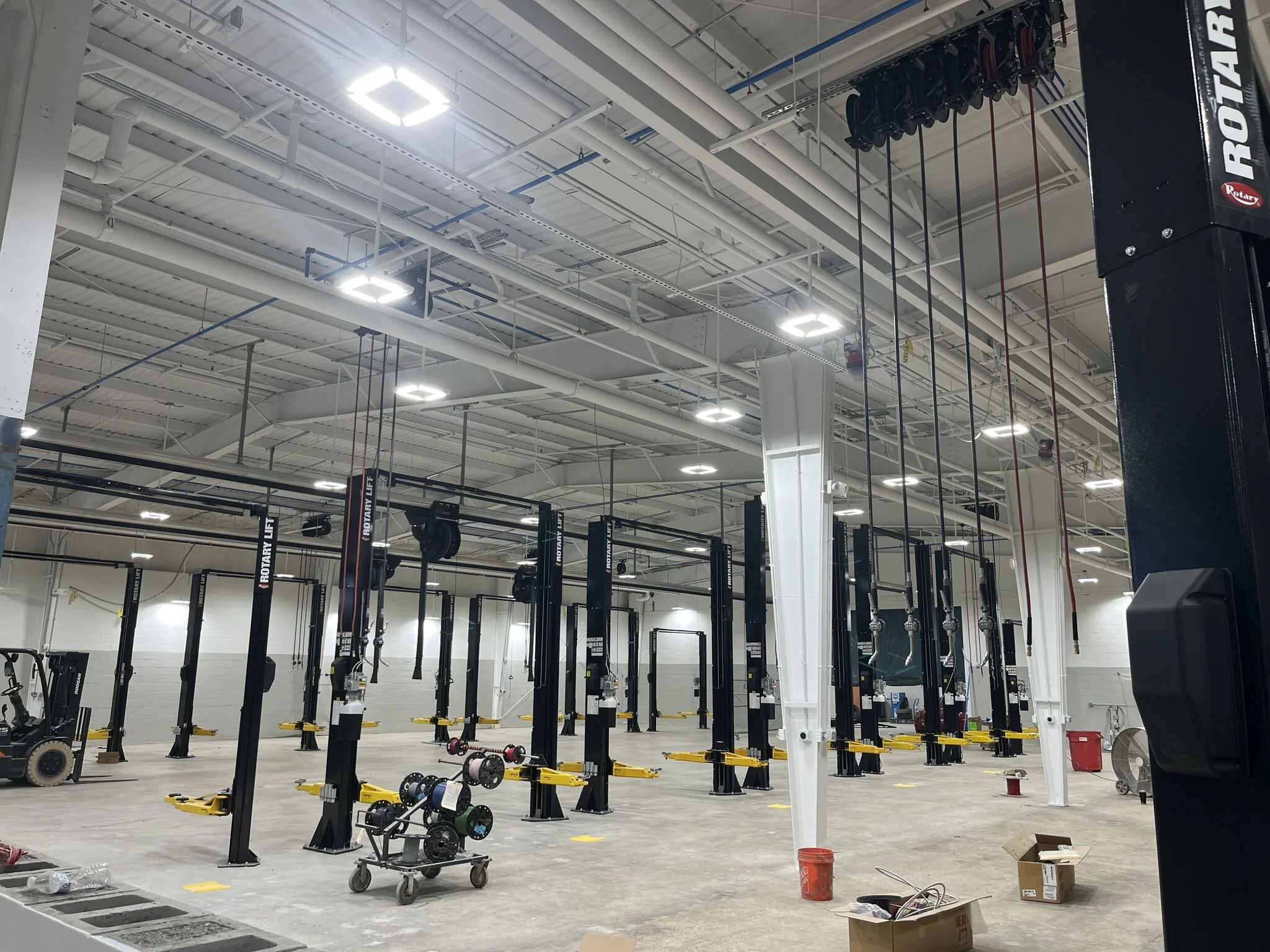Empty gym with weightlifting stations, barbells, and weights, as construction or setup is in progress.