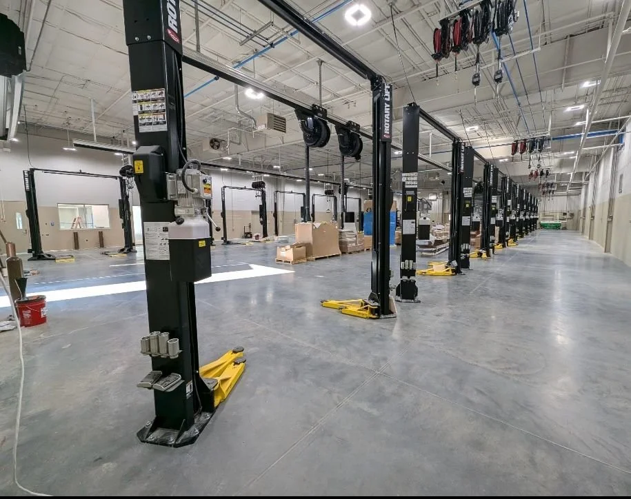 Empty automotive repair lift bays in a warehouse or garage with equipment hanging from the ceiling.
