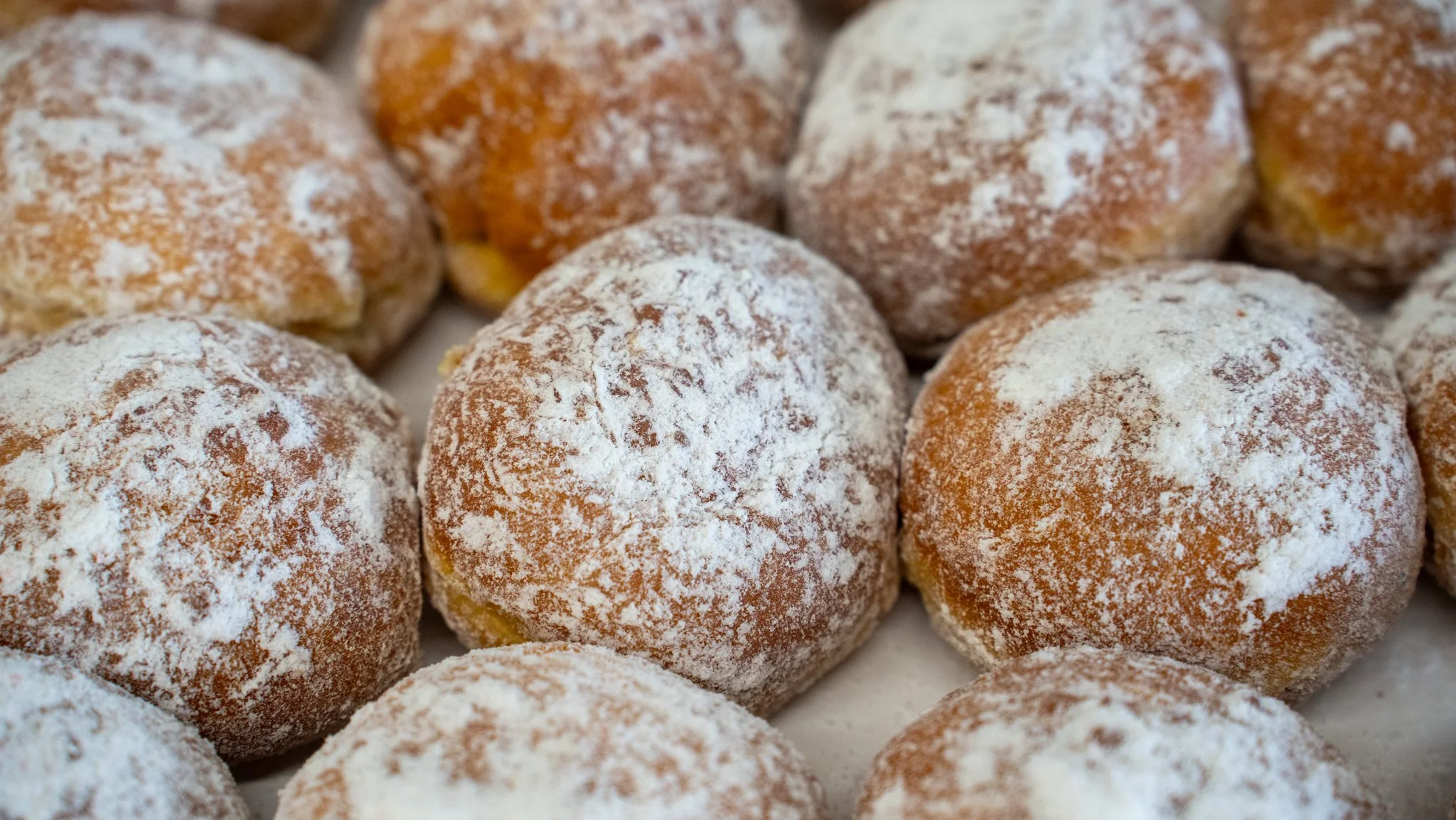 Close-up of powdered sugar-coated doughnuts arranged closely together.