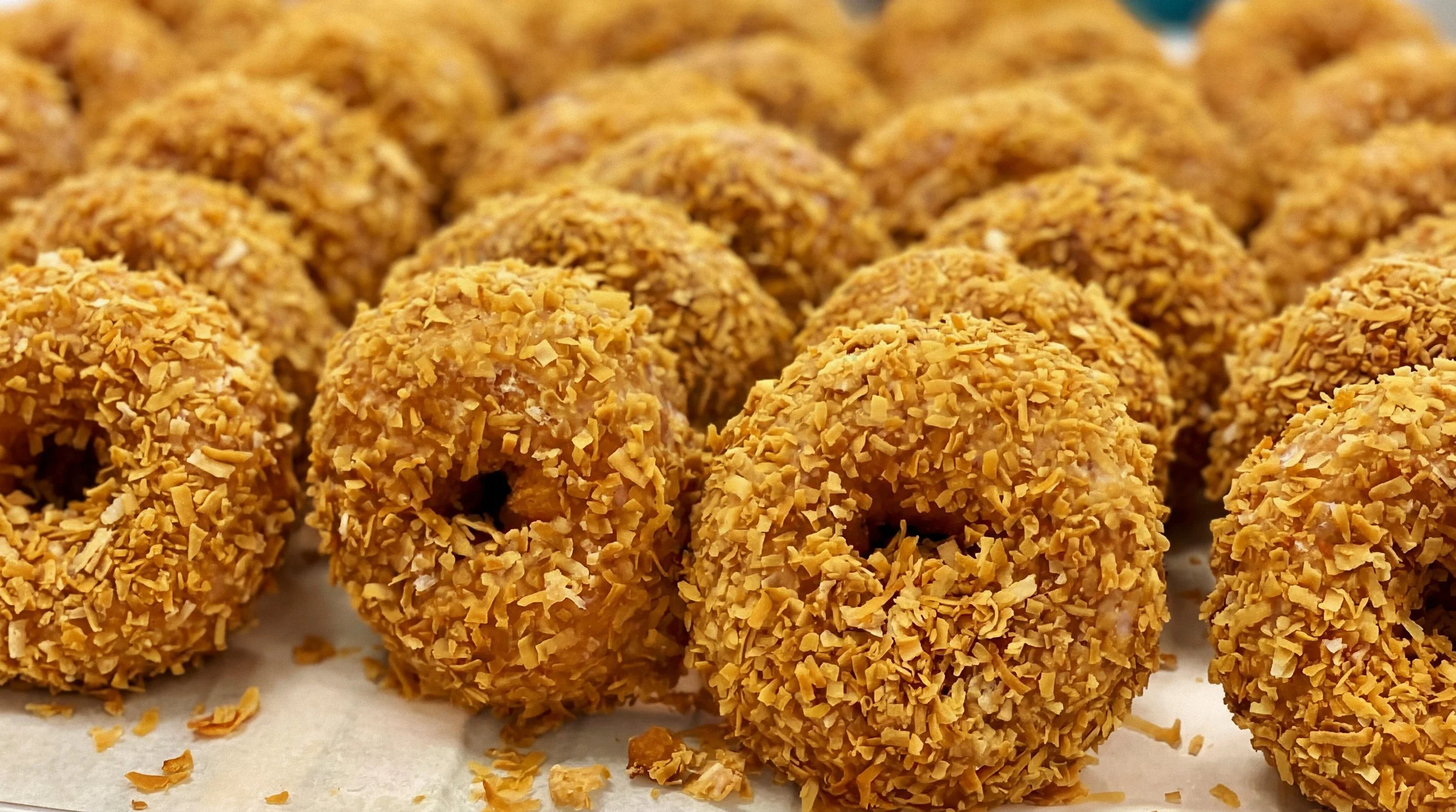 Close-up of multiple fried food balls coated with crushed nuts or breadcrumbs on a sheet of parchment paper.