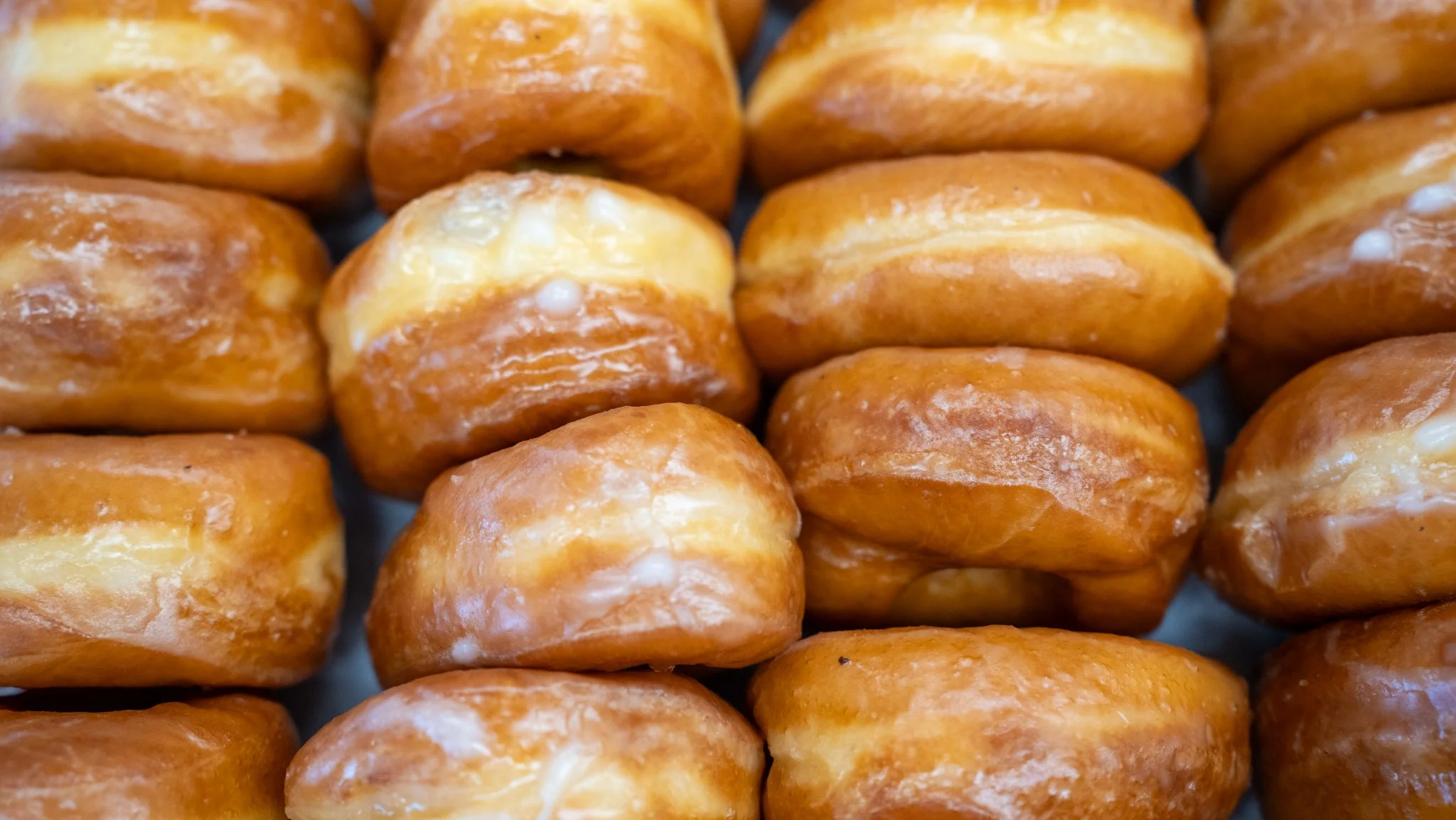 Close-up of glazed donuts with a shiny caramel-colored surface, arranged in rows.