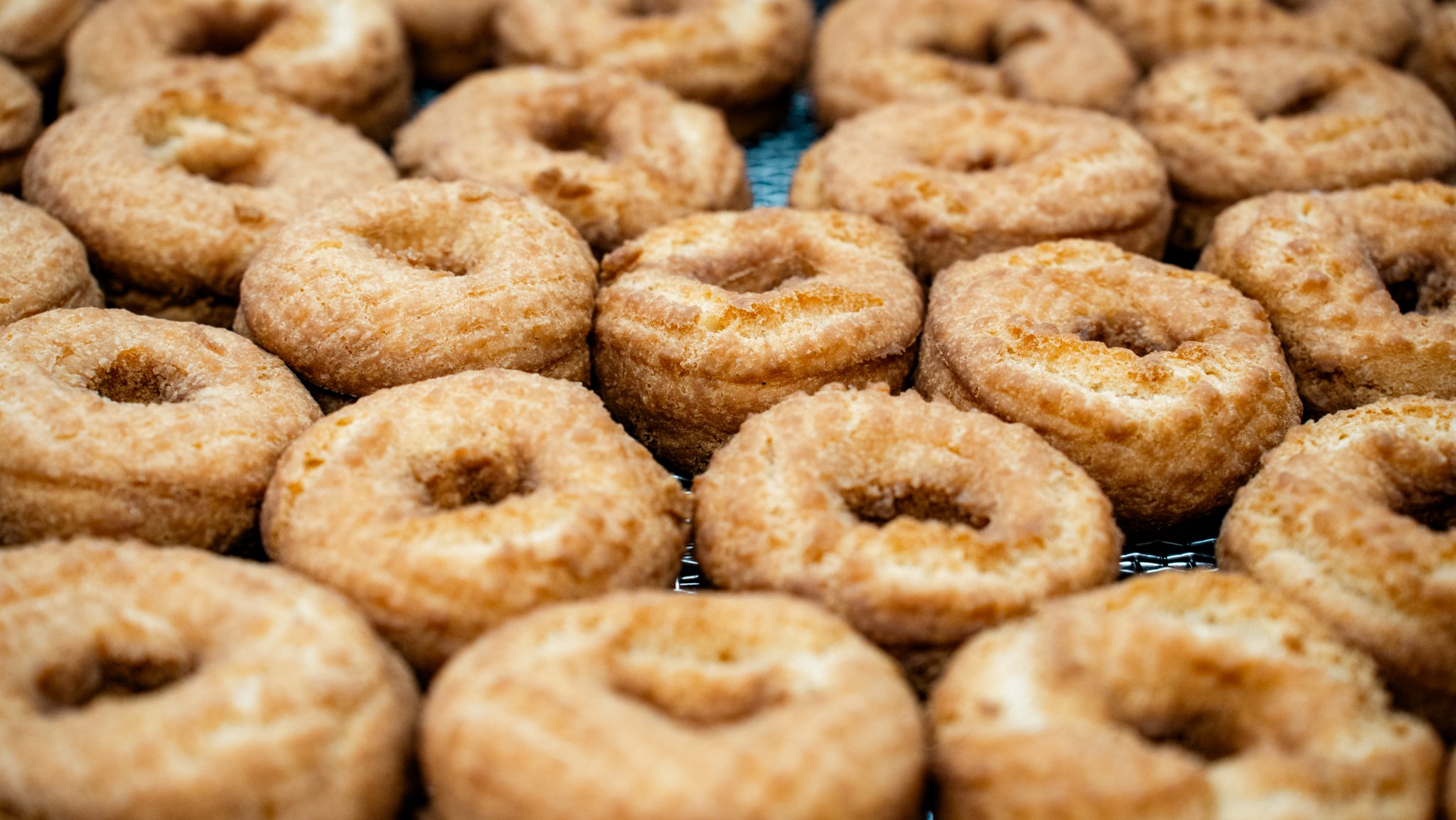 Close-up of many baked, glazed donuts with a hole in the center, arranged closely together on a cooling rack.