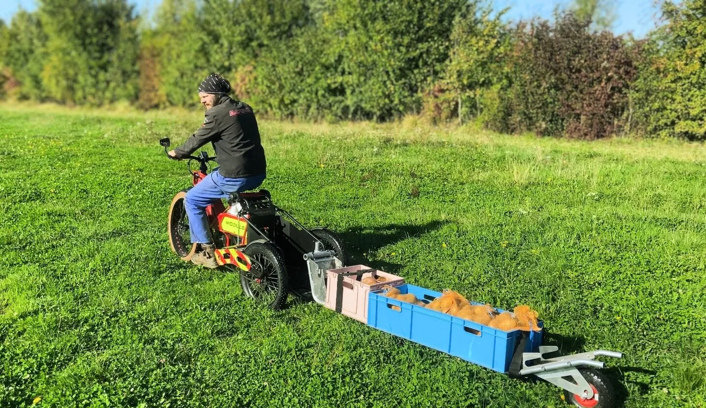 Agriculteur sur un vélo cargo dans son champs deplacant une remorque de pommes de terres