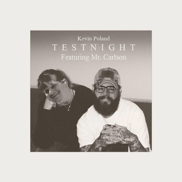Black and white photo of two people sitting at a table. One is a woman with dark hair, smiling, and the other is a man with a beard, glasses, a cap, and tattoos on his hands, also smiling. The background features text that reads "Kevin Poland TESTNIGHT Featuring Mr. Carlson."