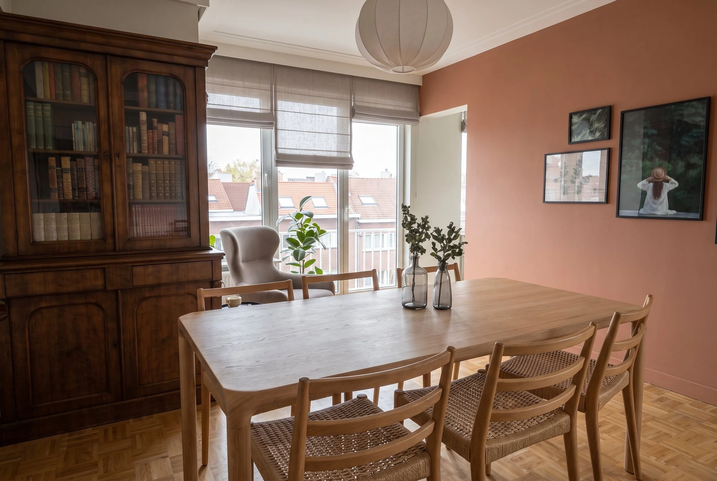 Salle à manger du projet Hoover avec grande table en bois, bibliothèque ancienne, mur terracotta décoré de cadres et vue dégagée.