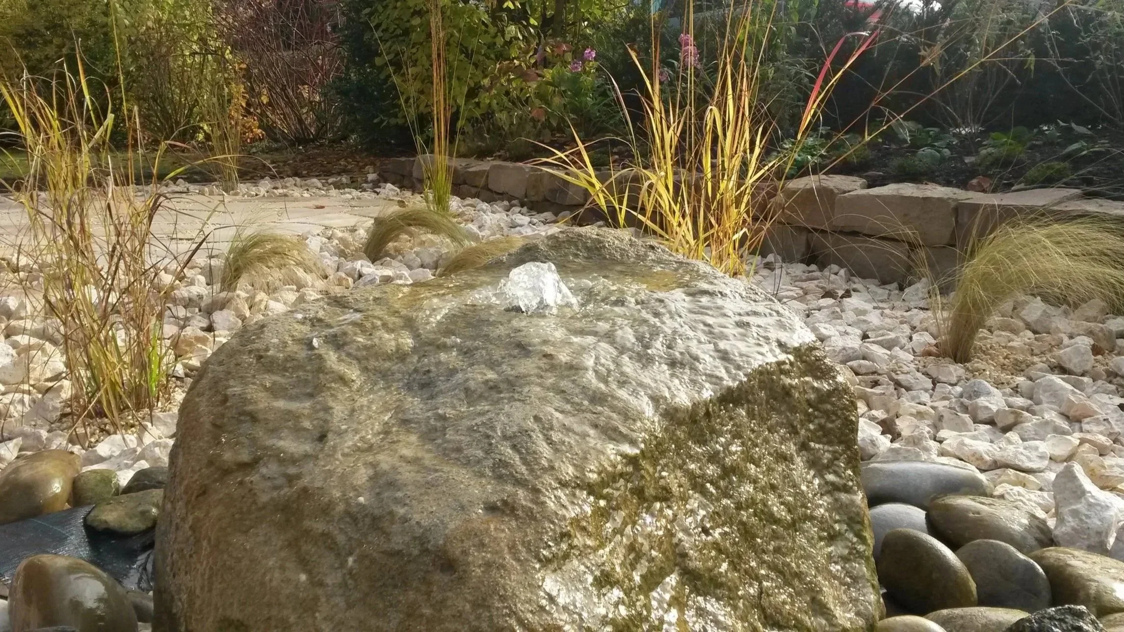 Naturnahe Gartengestaltung mit Findlingen, Wasserspiel, Kiesflächen und Bepflanzung