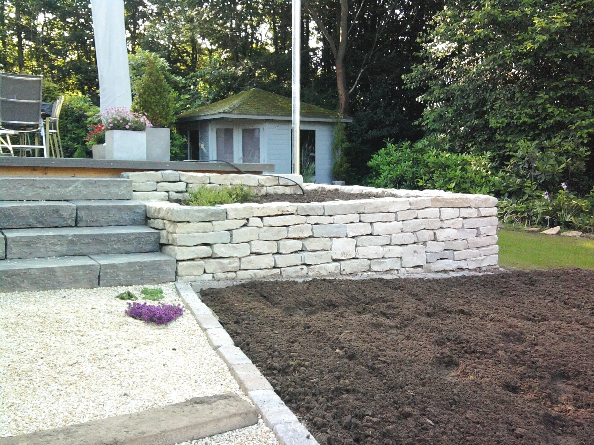 Gartengestaltung mit Natursteinmauer, Stufenanlage und bepflanztem Beet