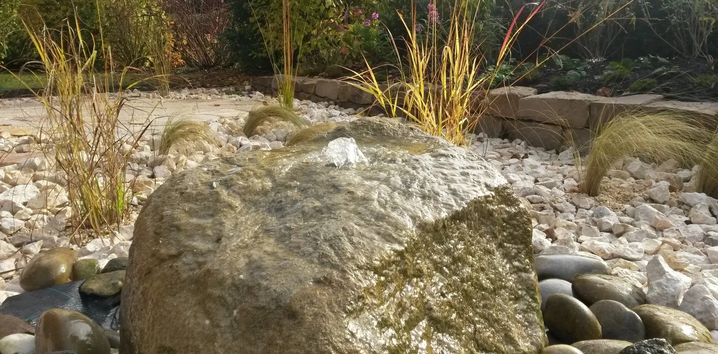Naturstein-Findling in modernem Steingarten mit Ziergräsern, Wasserspiel und Stauden