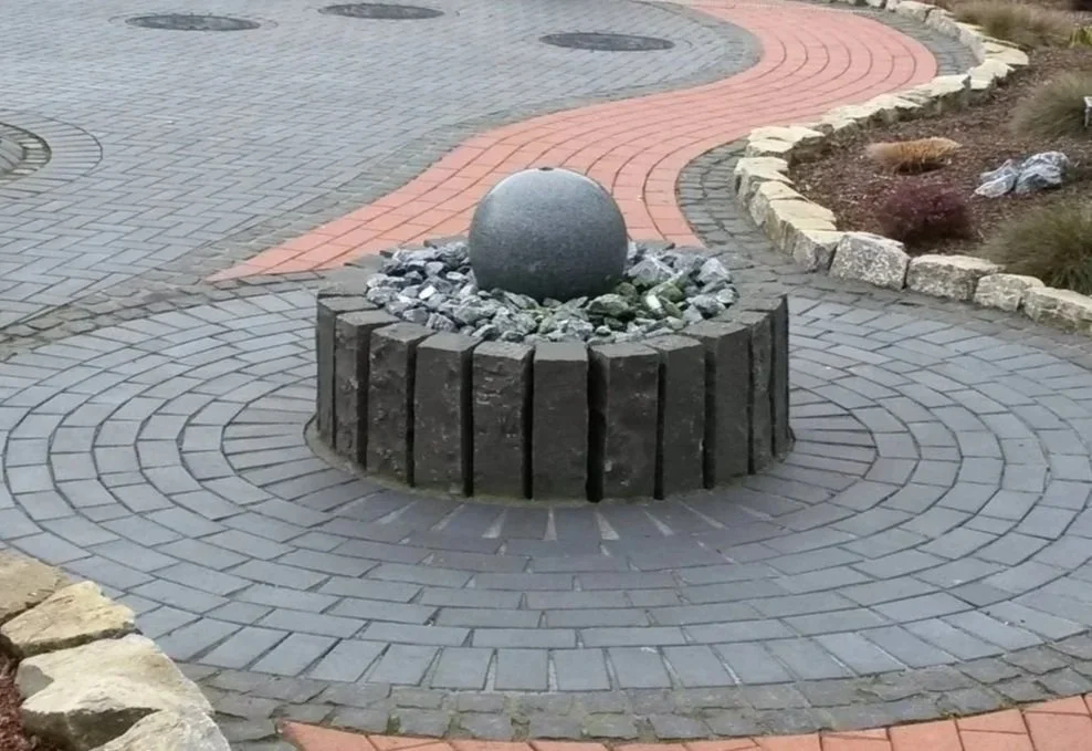 Runder Gartenbrunnen mit Granitkugel in gepflasterter Gartenanlage