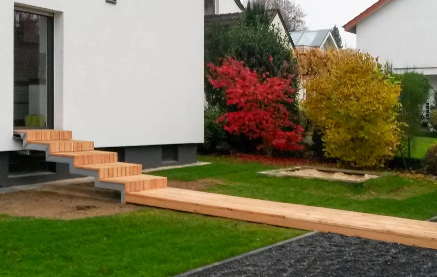 Holzsteg mit Treppe als Gartenzugang an modernem Wohnhaus