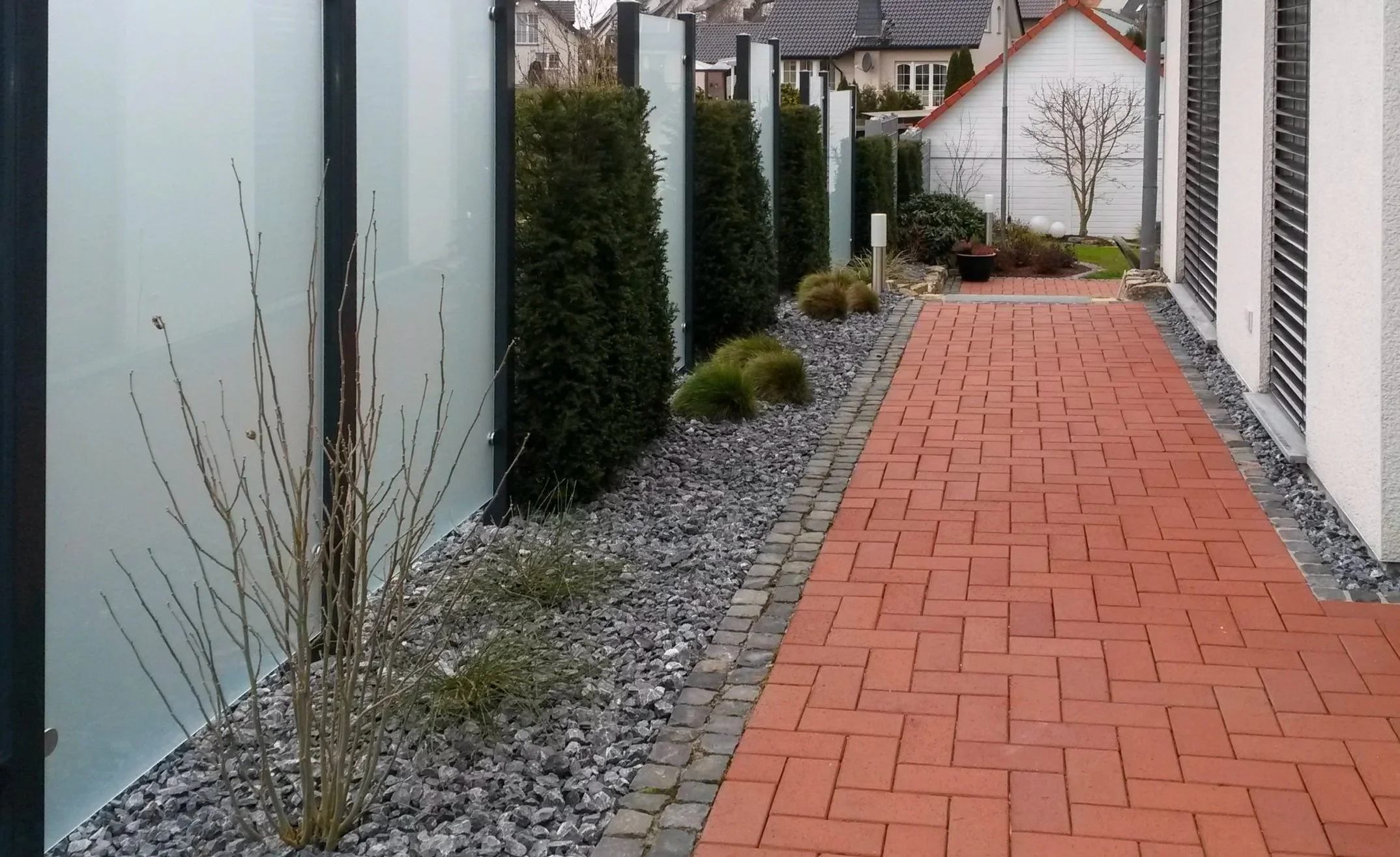 Gepflasterter Gehweg aus roten Betonsteinen mit Kiesbeet, Sichtschutz und Heckenbepflanzung
