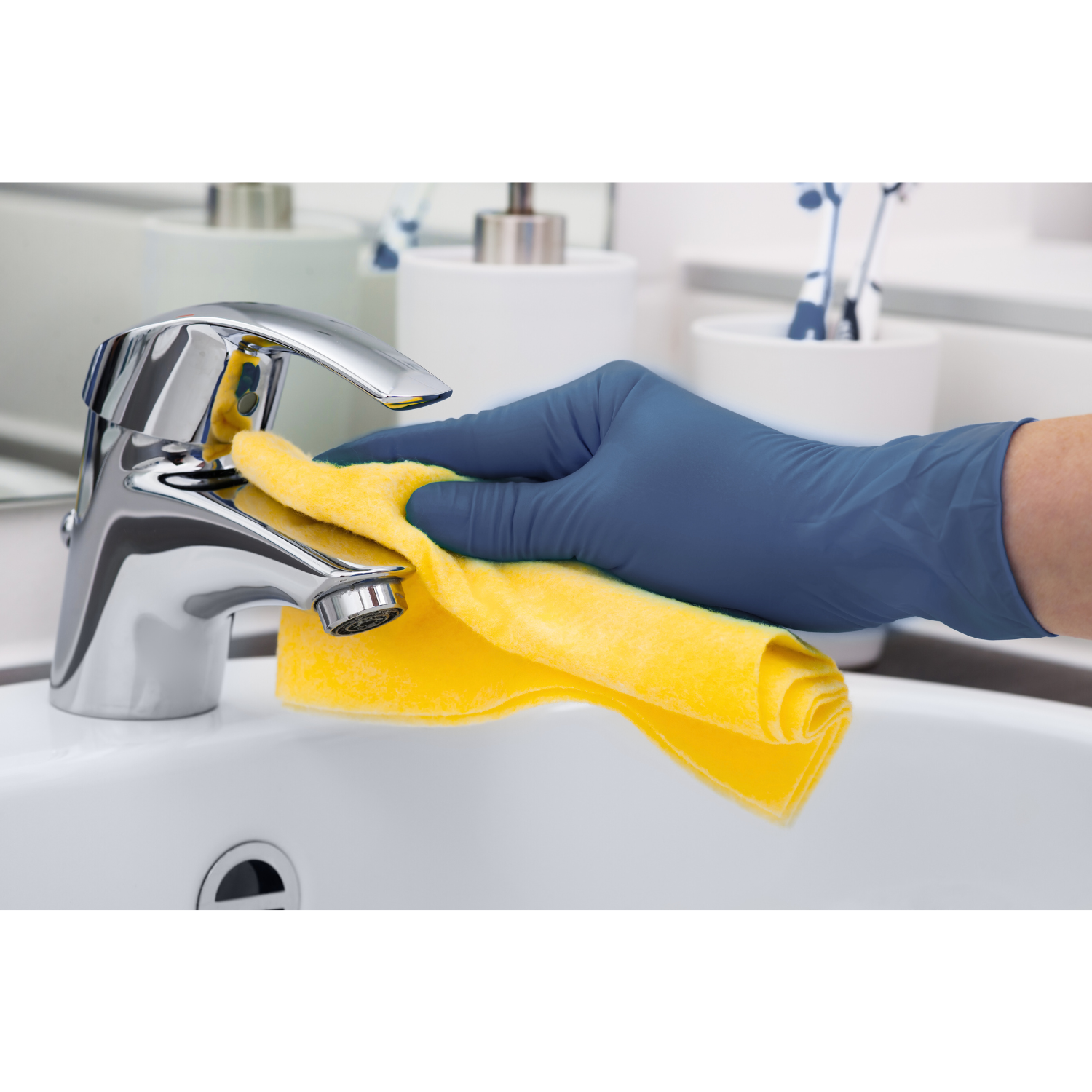Persona limpiando un grifo con un paño amarillo, usando guantes azules en un lavabo.