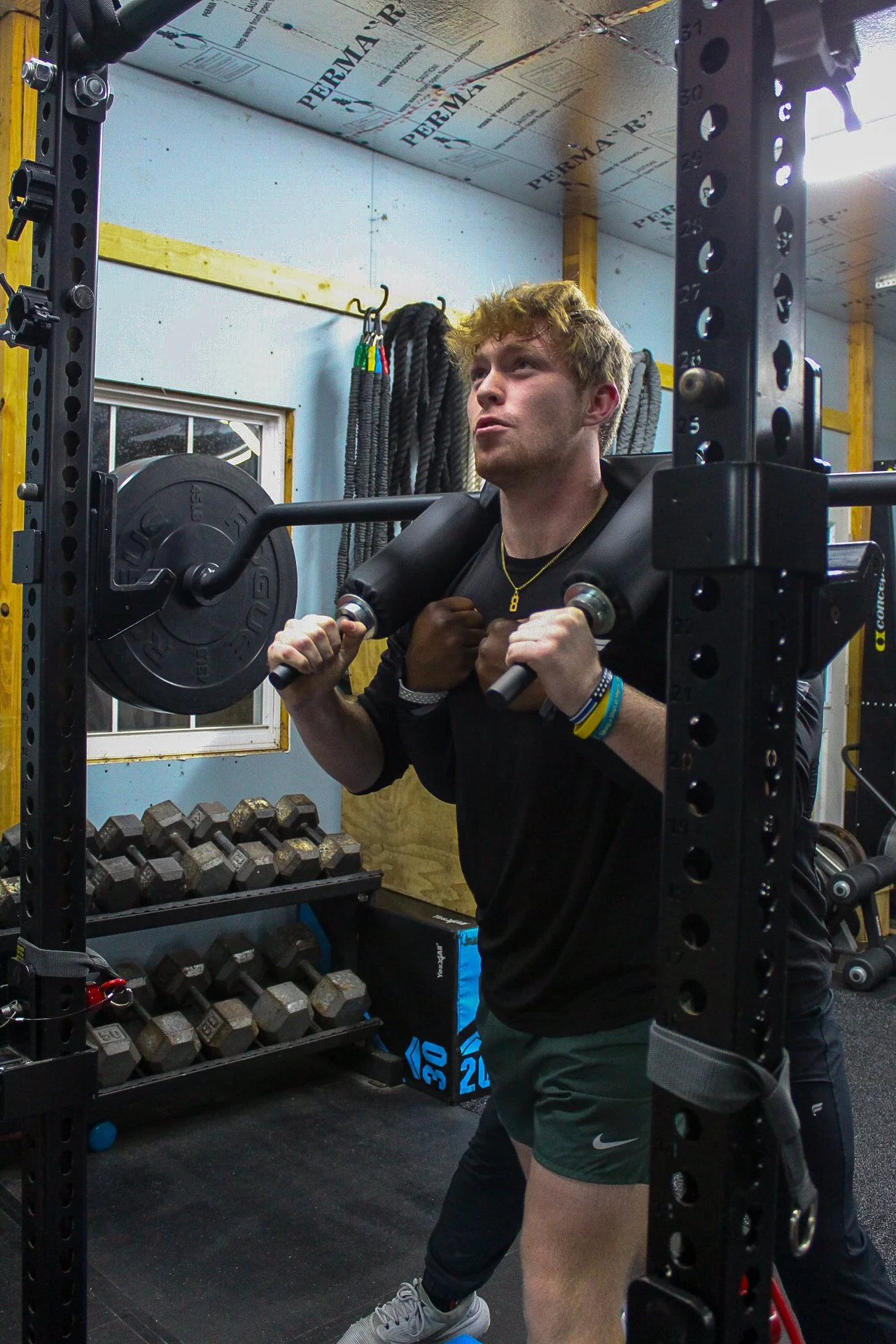 A young man performing a squat exercise with a weighted barbell across his shoulders in a gym.
