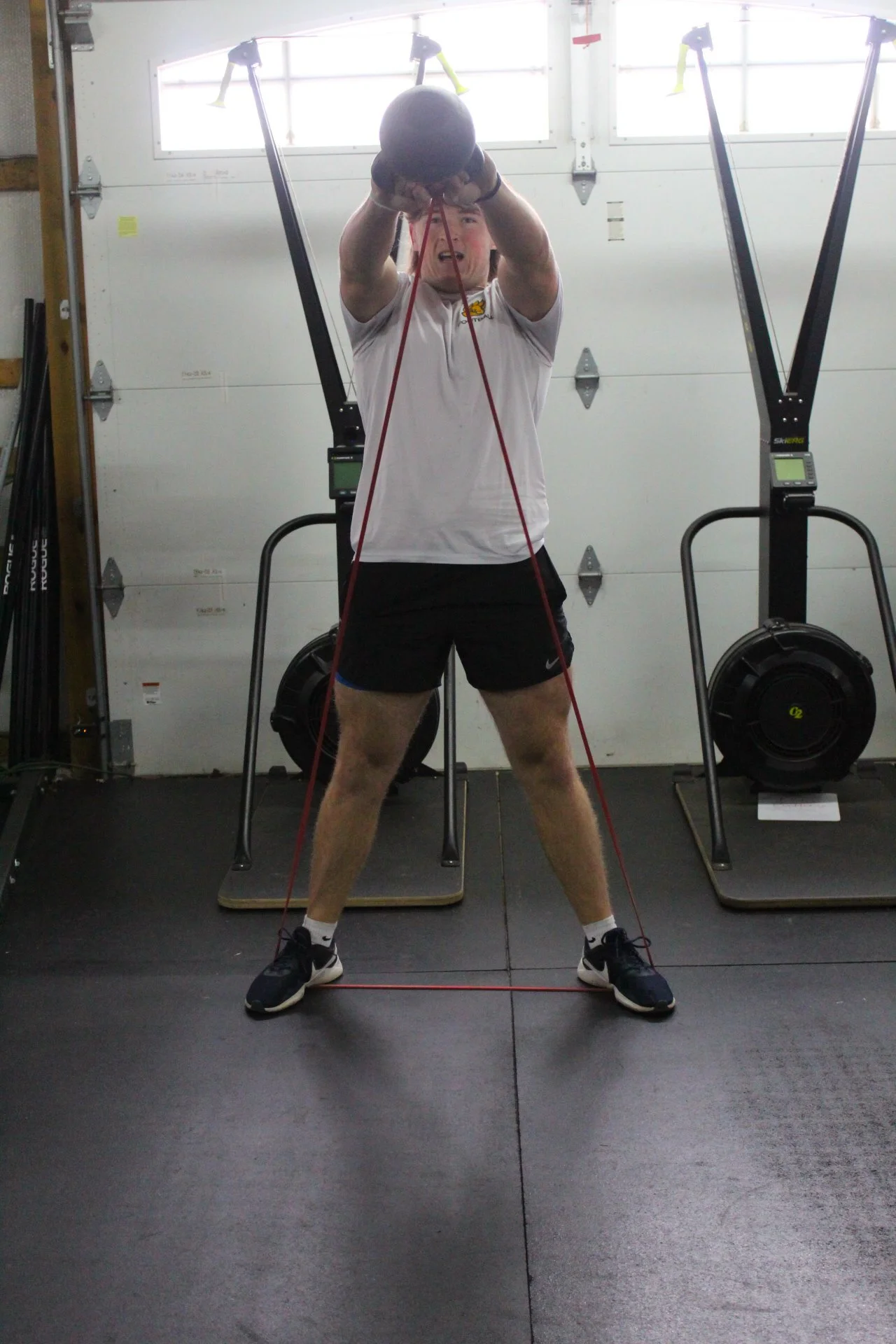 Man in white t-shirt and black shorts doing resistance band exercises in a gym.