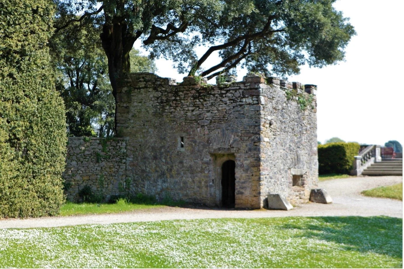 Colour photograph of the Blockhouse. This dates from c.  1545 and is listed II*. Green grass, tree , sky.