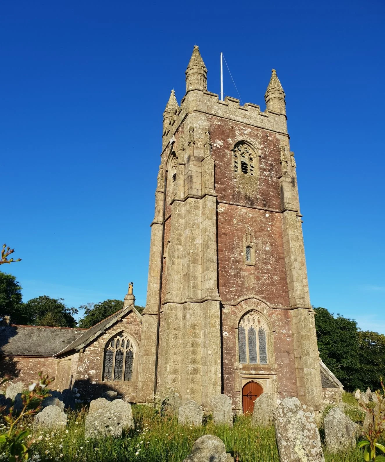 Historic Maker Church photographed looking up at the spire. on a sunny day. Old gravestones are visible at the bottom of the image.