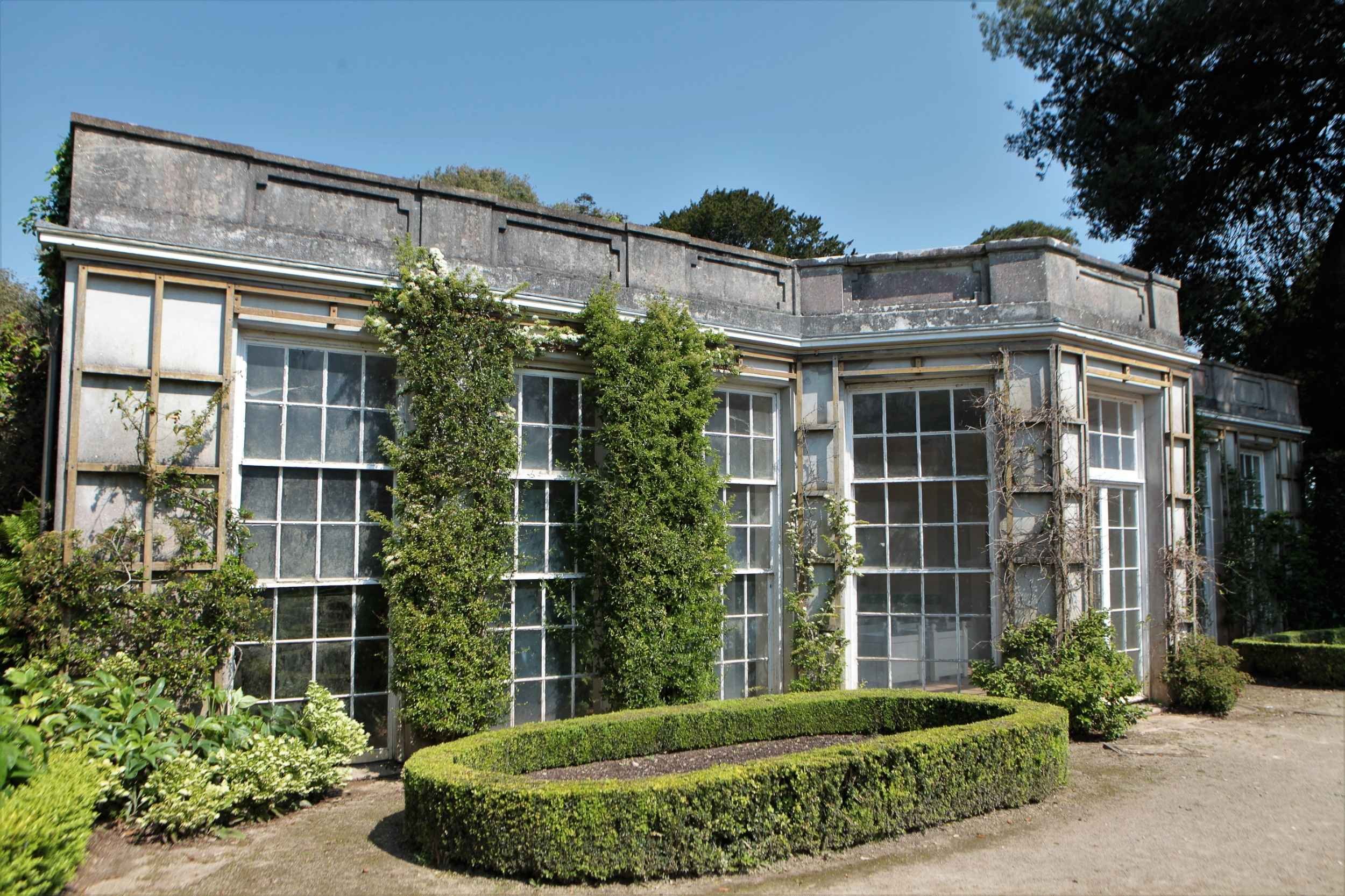 Colour photo of French Garden House, seen at an angle. Tall white painted windows.  Blue sky.