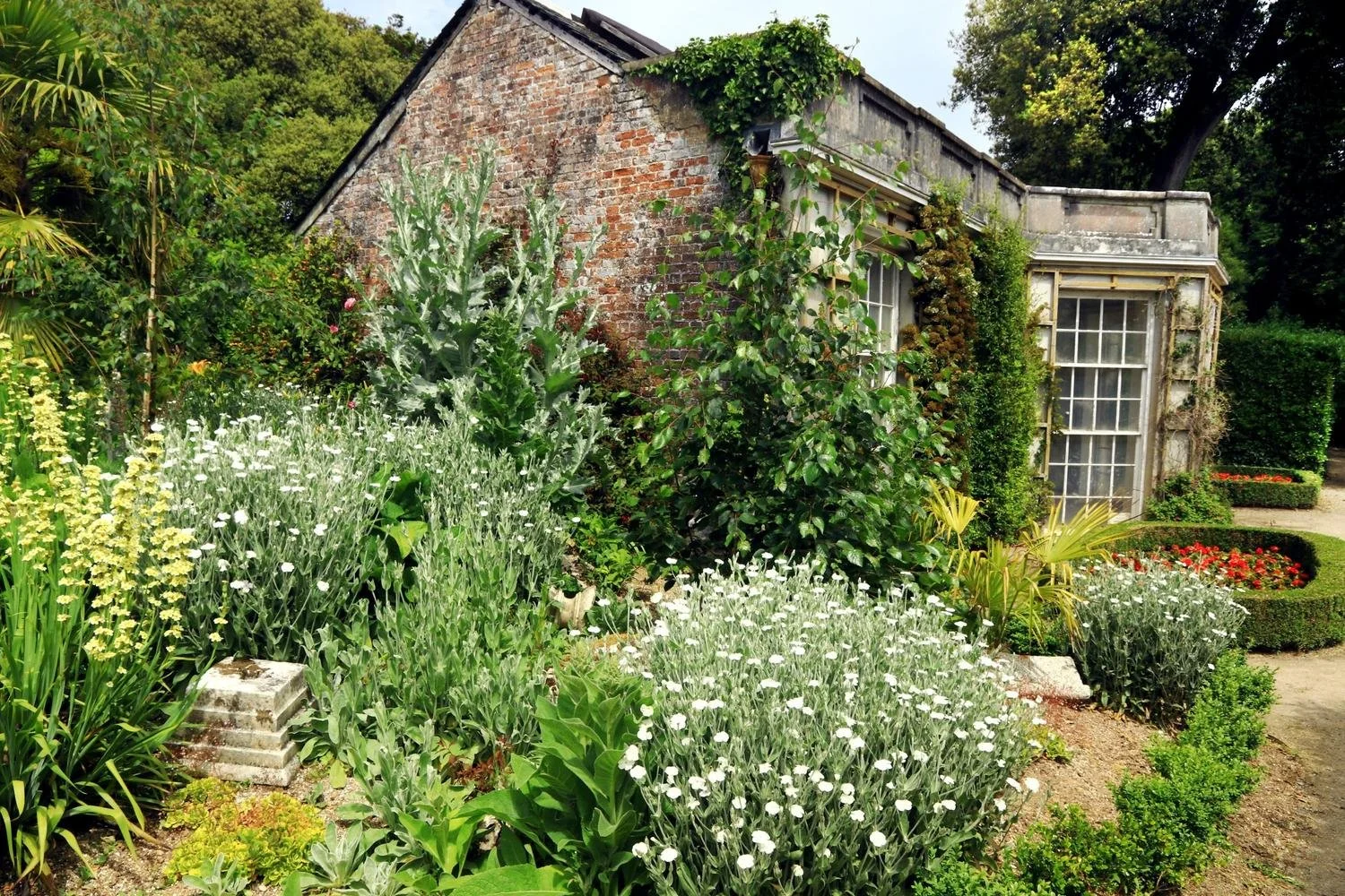 The French Garden House viewed from the side through a mass of foliage. Side of building constructed from small red bricks.