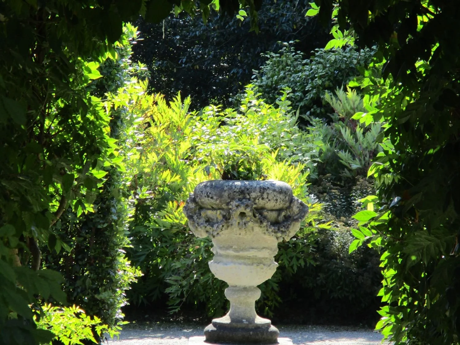 Urn erected to the memory of Sophia Edgcumbe (née Hobart) after her early death in 1806.  Urn is in dappled sunlight framed by luminous foliage from hedges bordering paths.