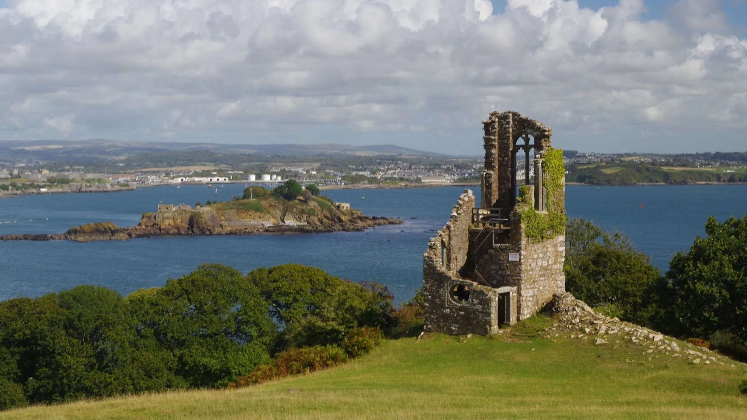 Photo of Folly against backdrop of Drake's Island and Plymouth. Sun, blue sea, hazy blue sky.