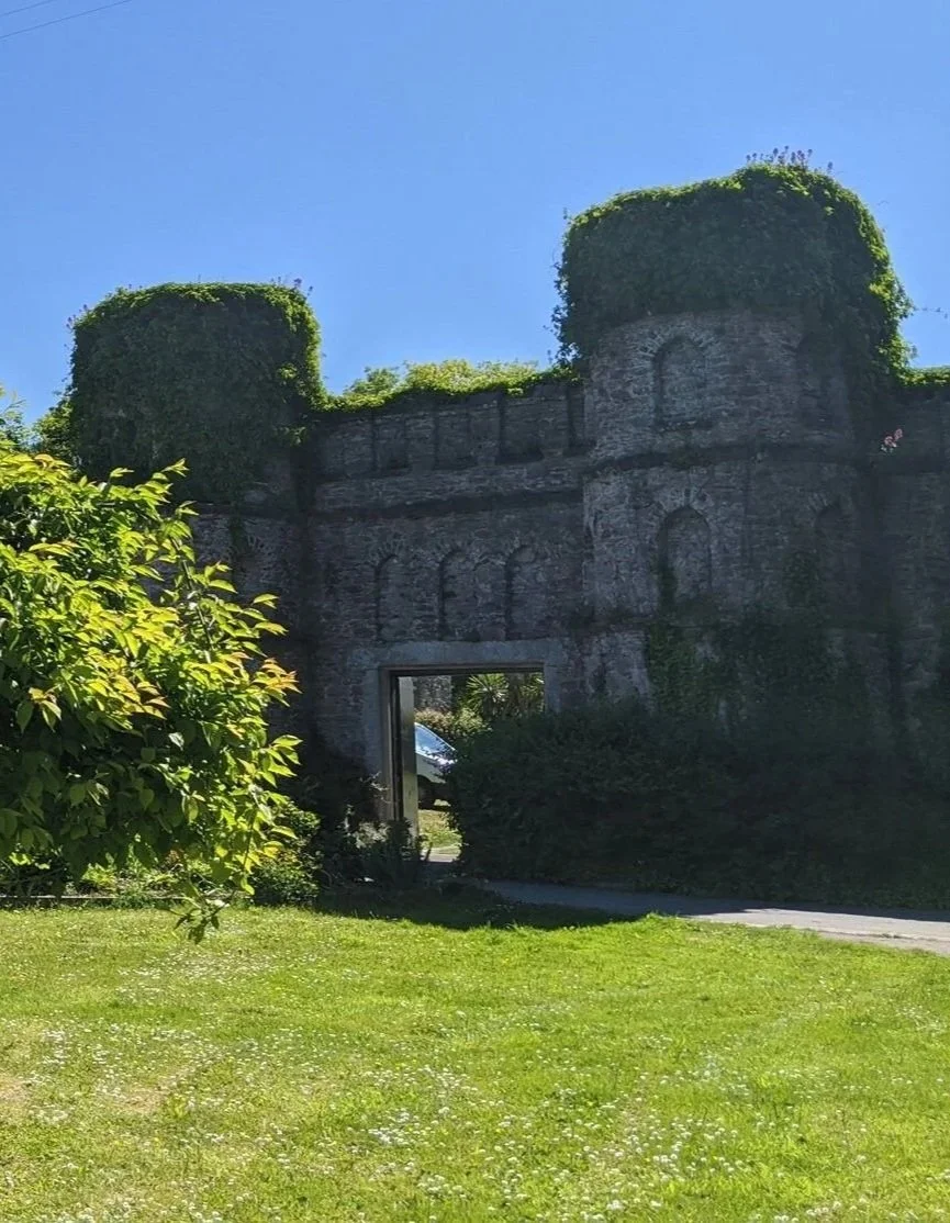 Photo of castellated folly wall at Empacombe. Green grass, blue sky, tree frames shot.