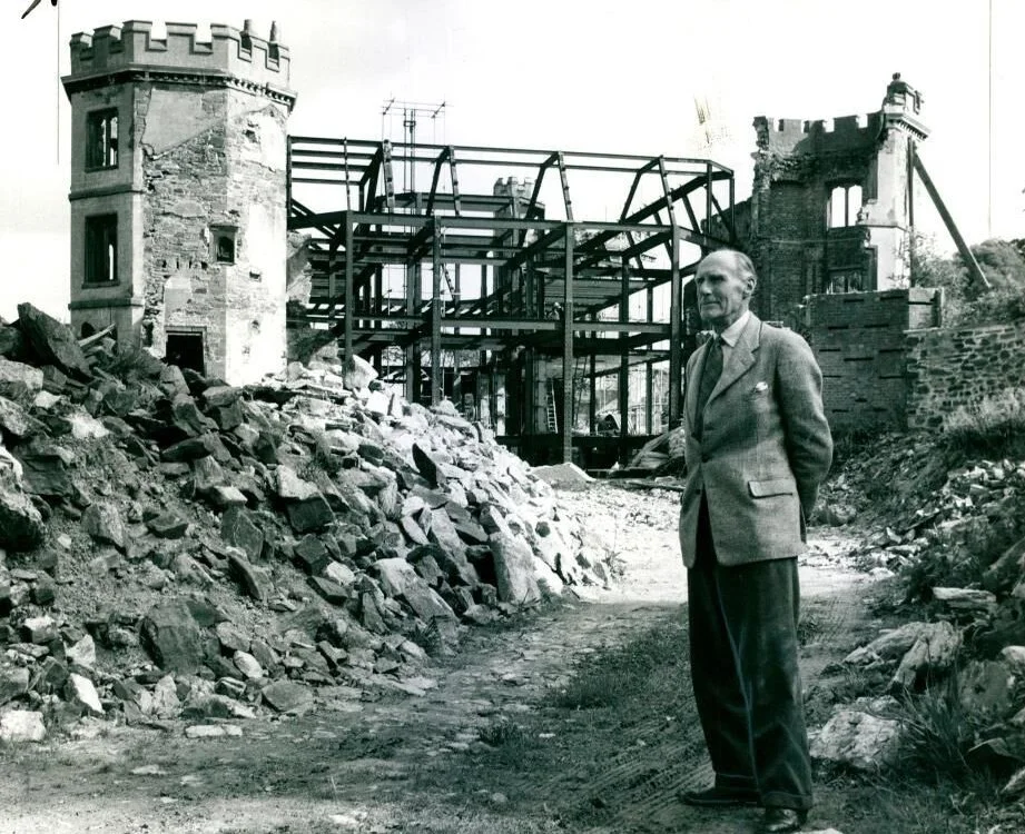 Black and white photograph of Kenelm Edgcumbe surveys destruction of Mount Edgcumbe House during restoration. c. 1958-59. Behind him are the ruins of the house.