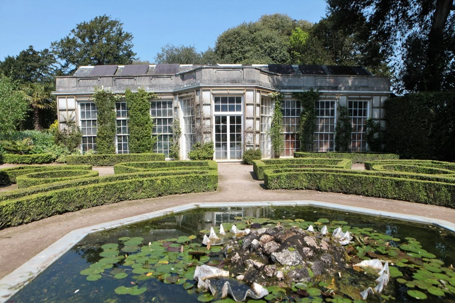French Garden House in 2023 from front with formal rococo pond and waterlilies in front. Trees, sun and blue sky.