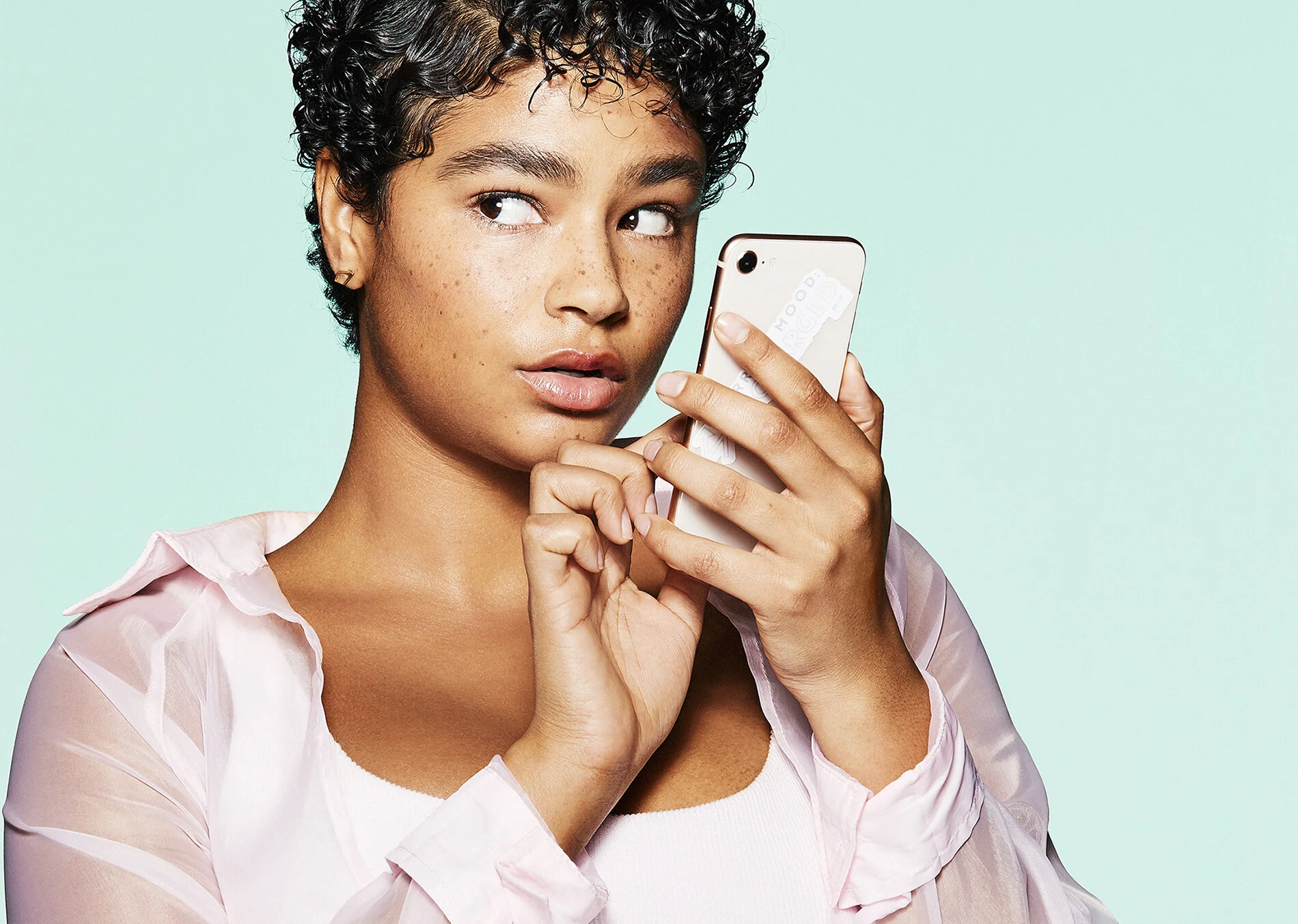 Young woman with short curly hair looking at a smartphone against a light turquoise background