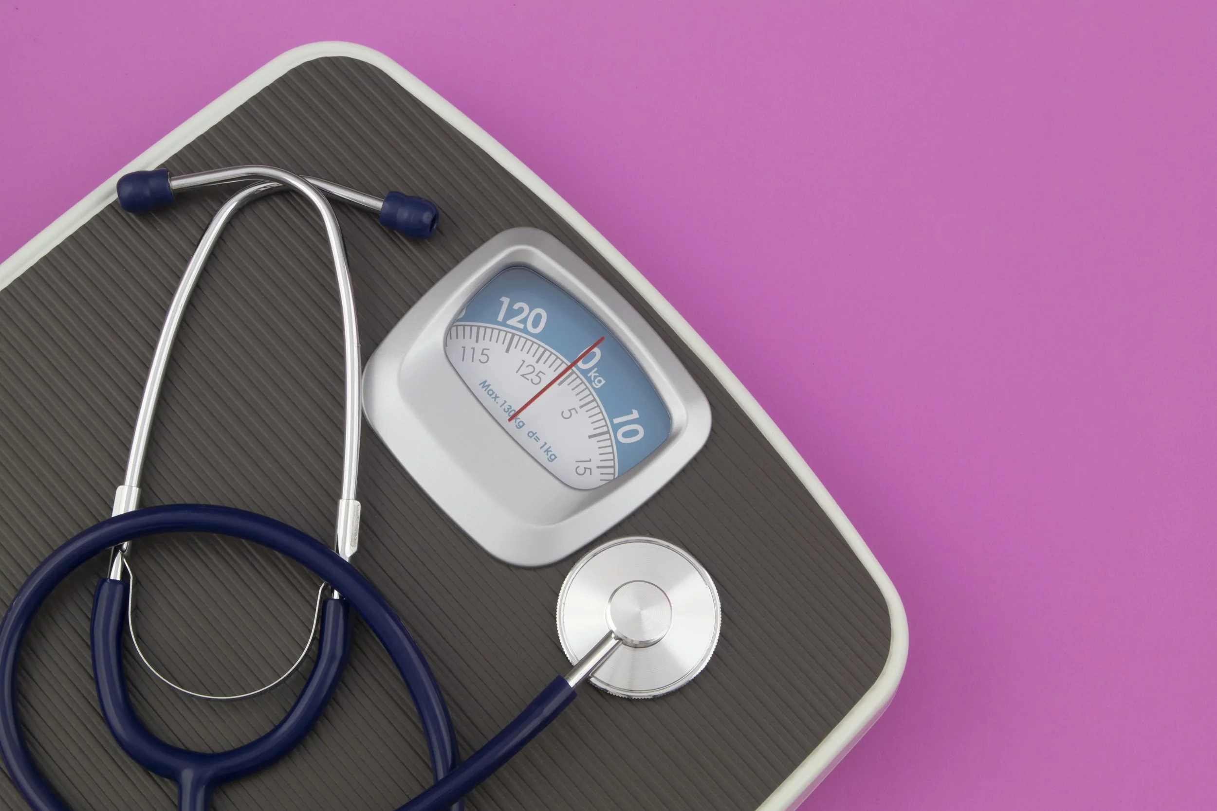 Scale with a stethoscope on top of it, set against a pink background