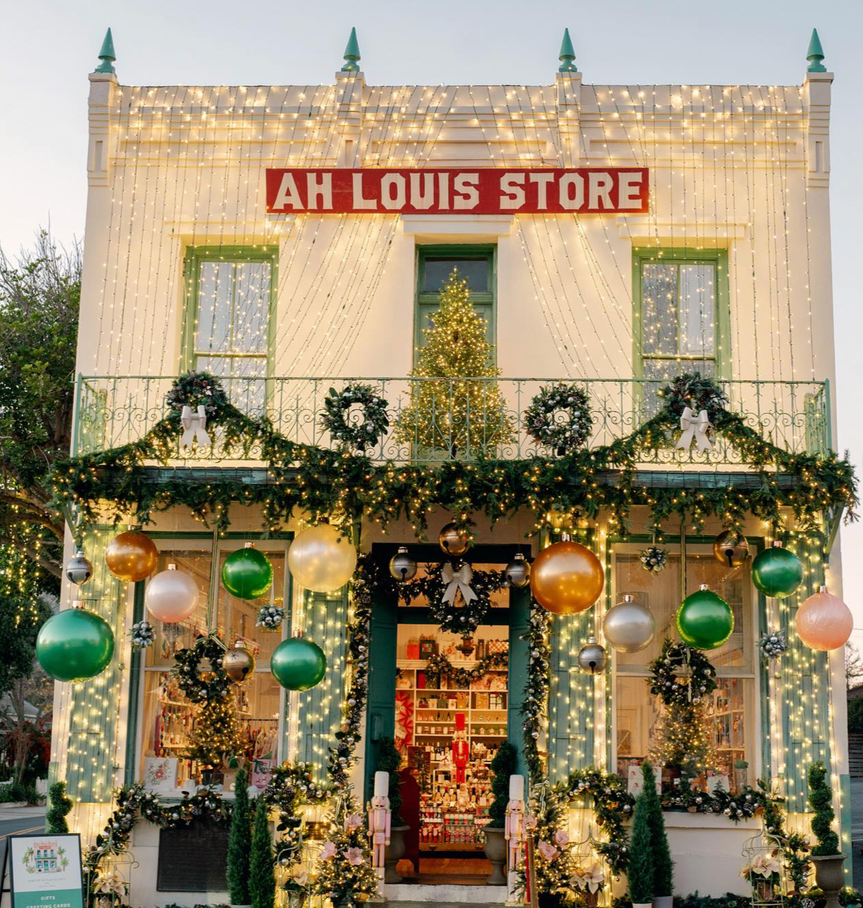 Two-story building decorated with Christmas lights, wreaths, and ornaments, with a sign that reads 'AH Louis Store.' The storefront has a Christmas tree, wreaths, and gold, green, and white ornaments, with festive garlands and string lights adorning