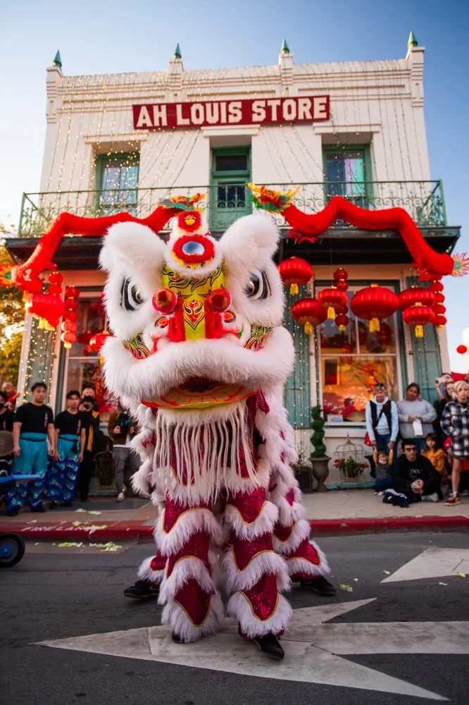 A traditional Chinese lion dance costume performing in front of a building decorated for a celebration.