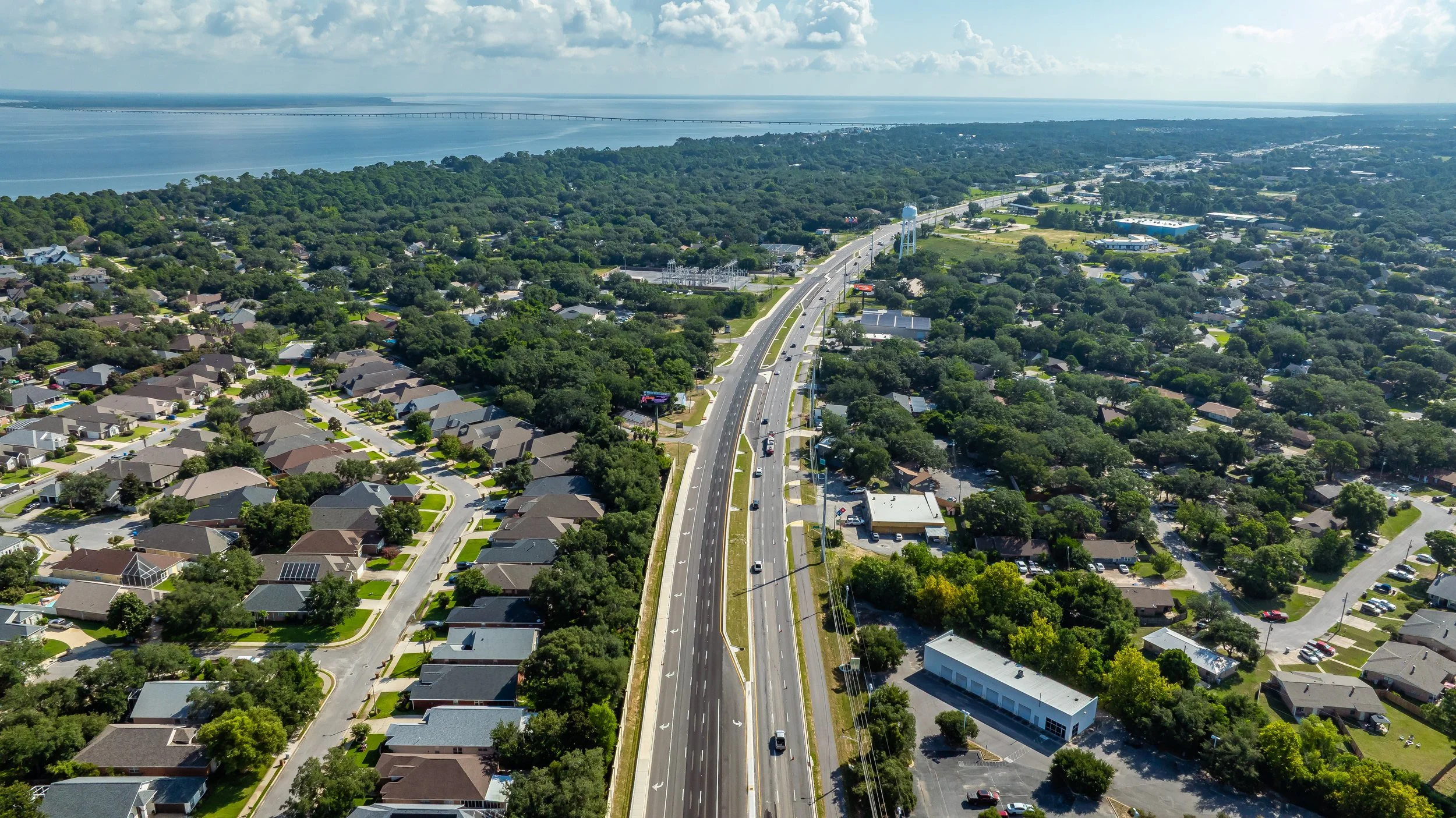 Aerial view of a residential neighborhood and highway near a body of water and a bridge in the distance.