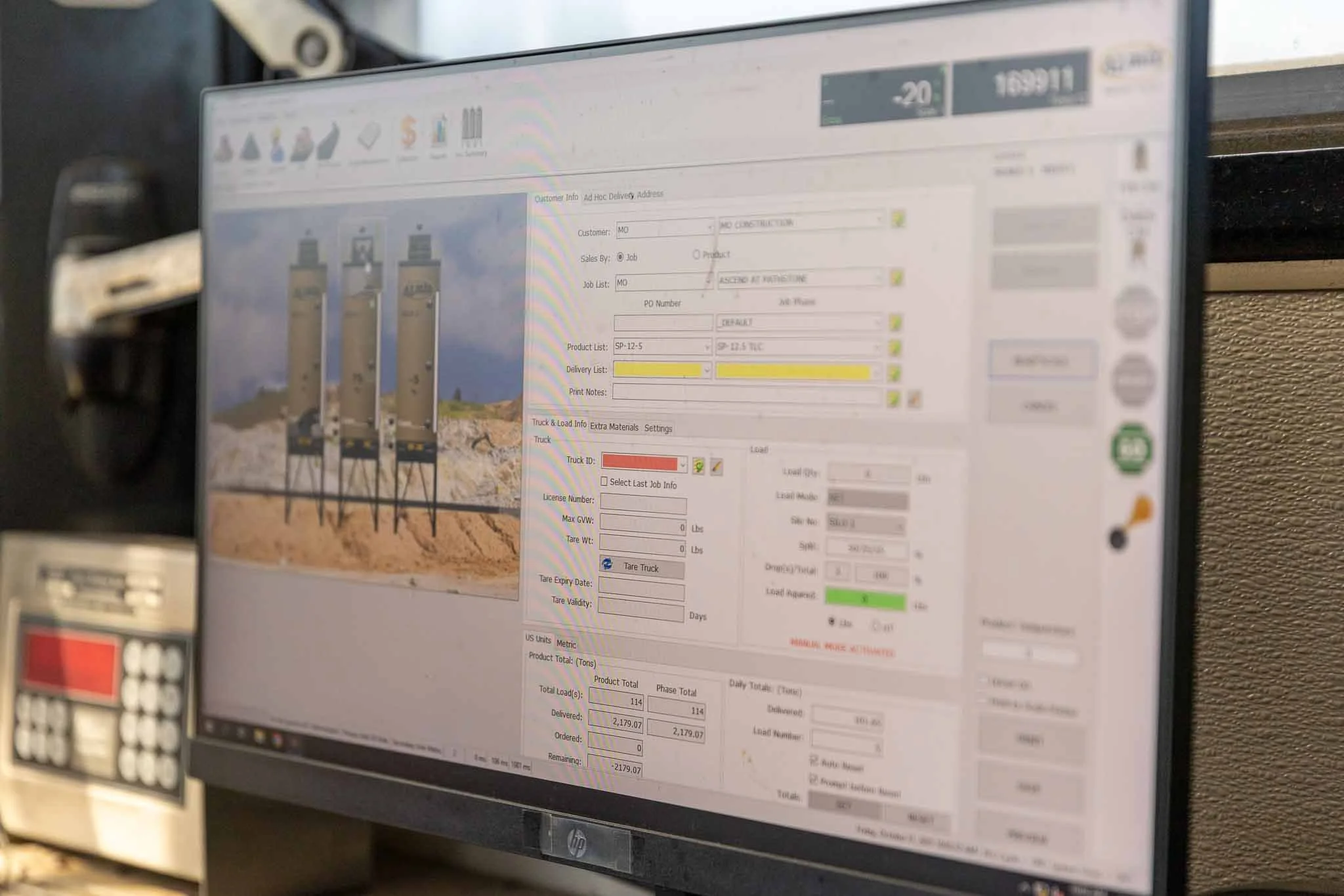 Computer monitor displaying a construction management software with a photo of three large industrial tanks at a construction site on the screen.