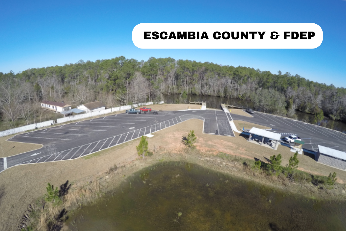 Aerial view of an empty parking lot with several cars, surrounded by trees and a small pond, with the text 'Escambia County & FDEP' overlaid.