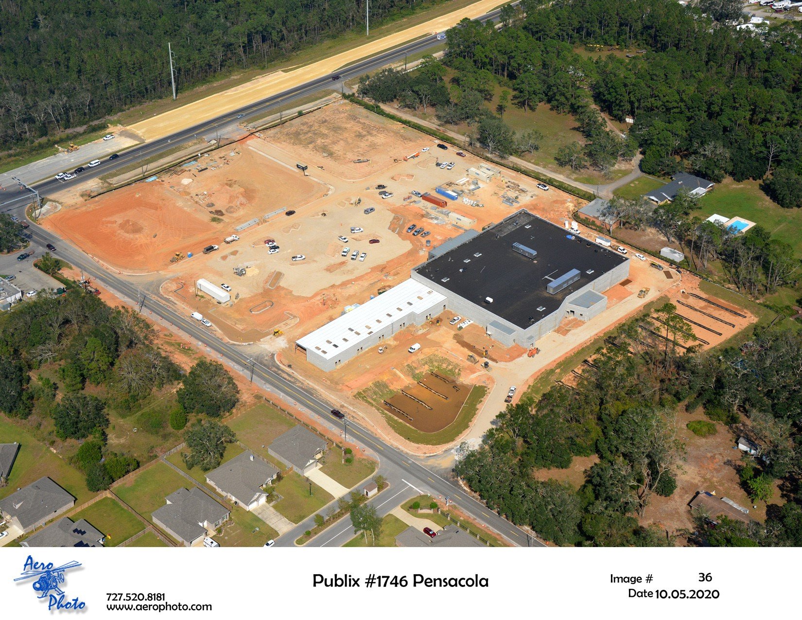Aerial view of a construction site for a new Publix supermarket in Pensacola, Florida, showing building structures, construction vehicles, and surrounding residential area.