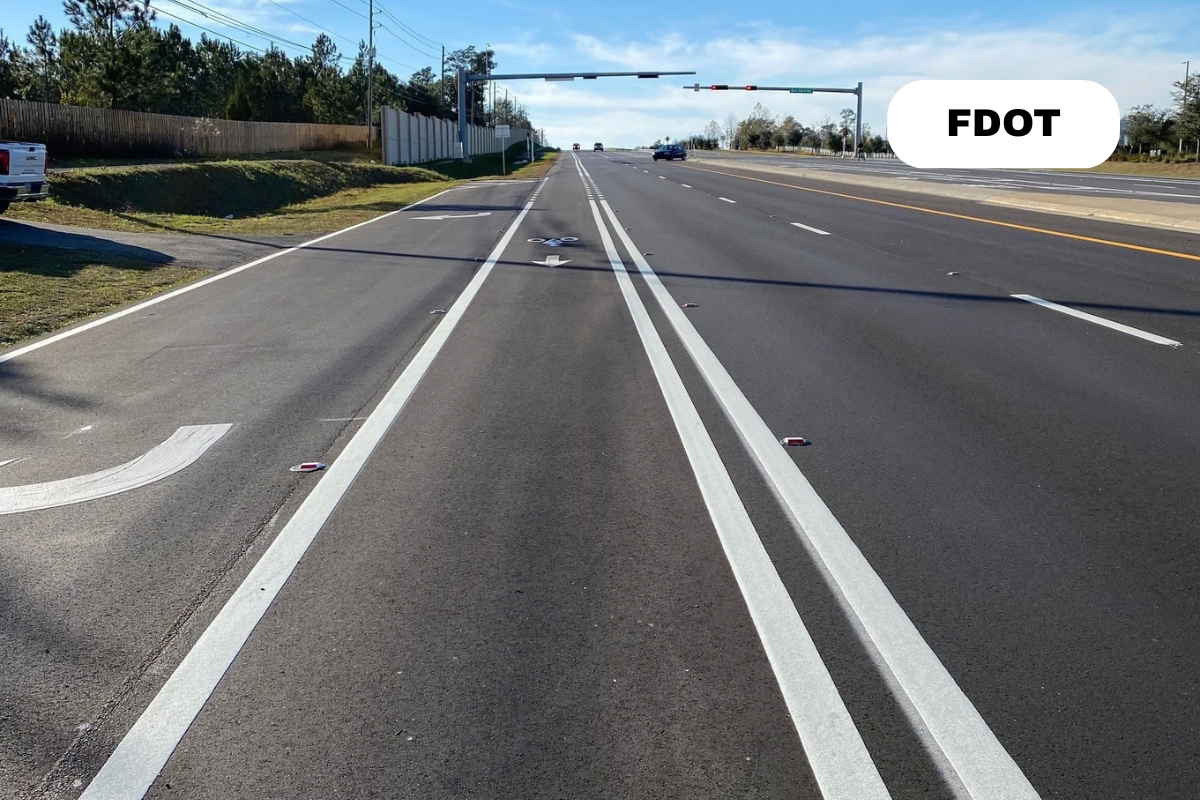 A bike lane on a highway with a Florida Department of Transportation (FDOT) sign, traffic signals, and multiple lanes of traffic.