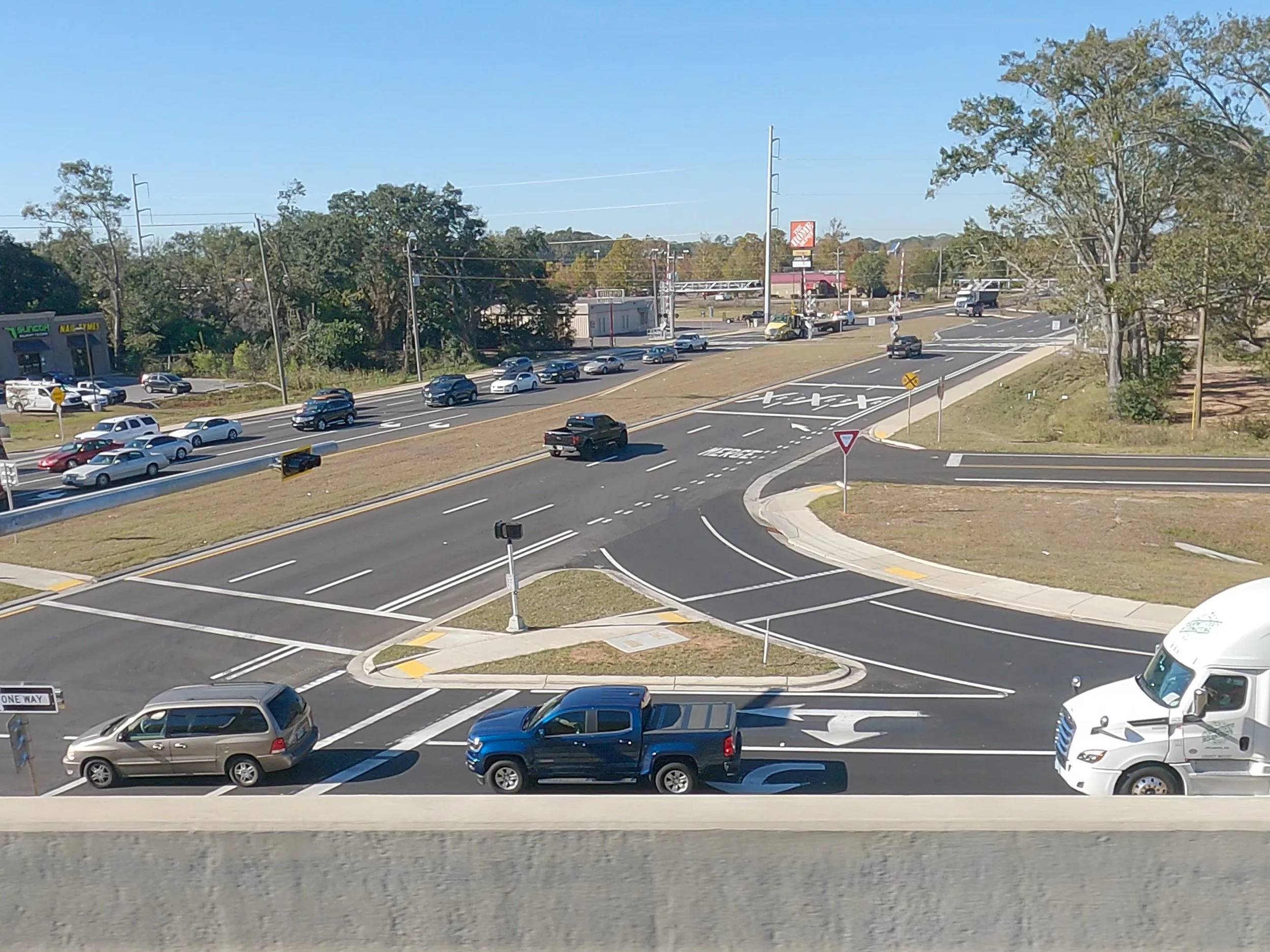 Multiple cars are on a multi-lane road with a curved intersection, leafless trees, and commercial buildings in the background.