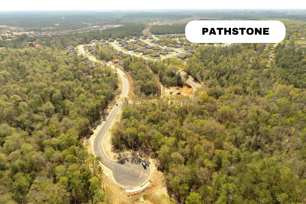 Aerial view of a winding road under construction in a wooded area leading to a neighborhood of newly built houses labeled 'Pathstone'.