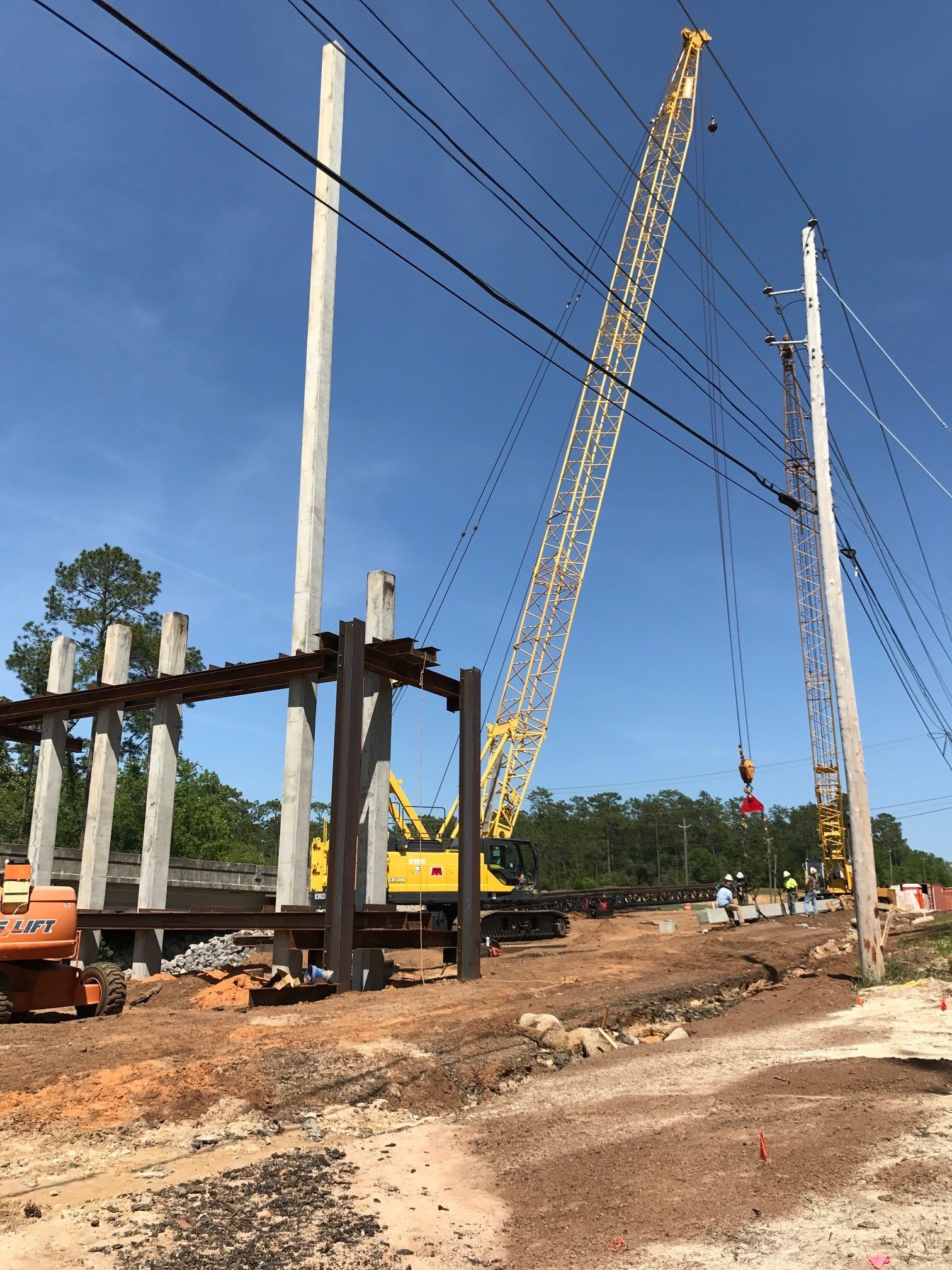 Construction workers working on a power line project with large cranes and utility poles during daytime.