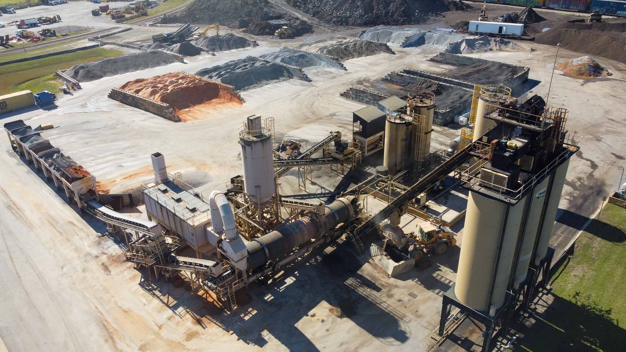 An industrial construction site with various machinery, conveyor belts, and piles of materials in an open area, likely for processing or manufacturing.