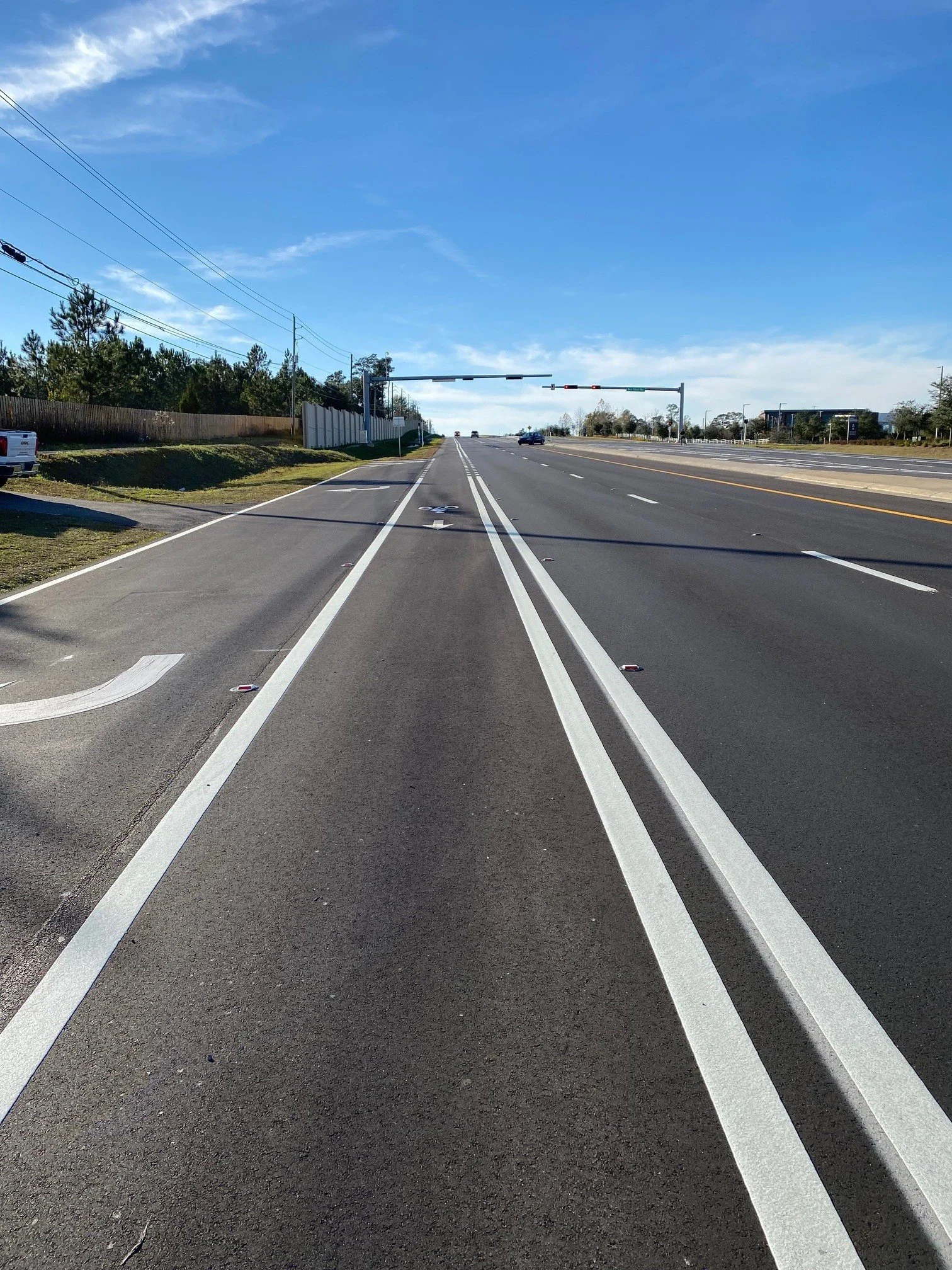 Empty road with dedicated bike lanes on each side, clear sky, and traffic signals in the distance.