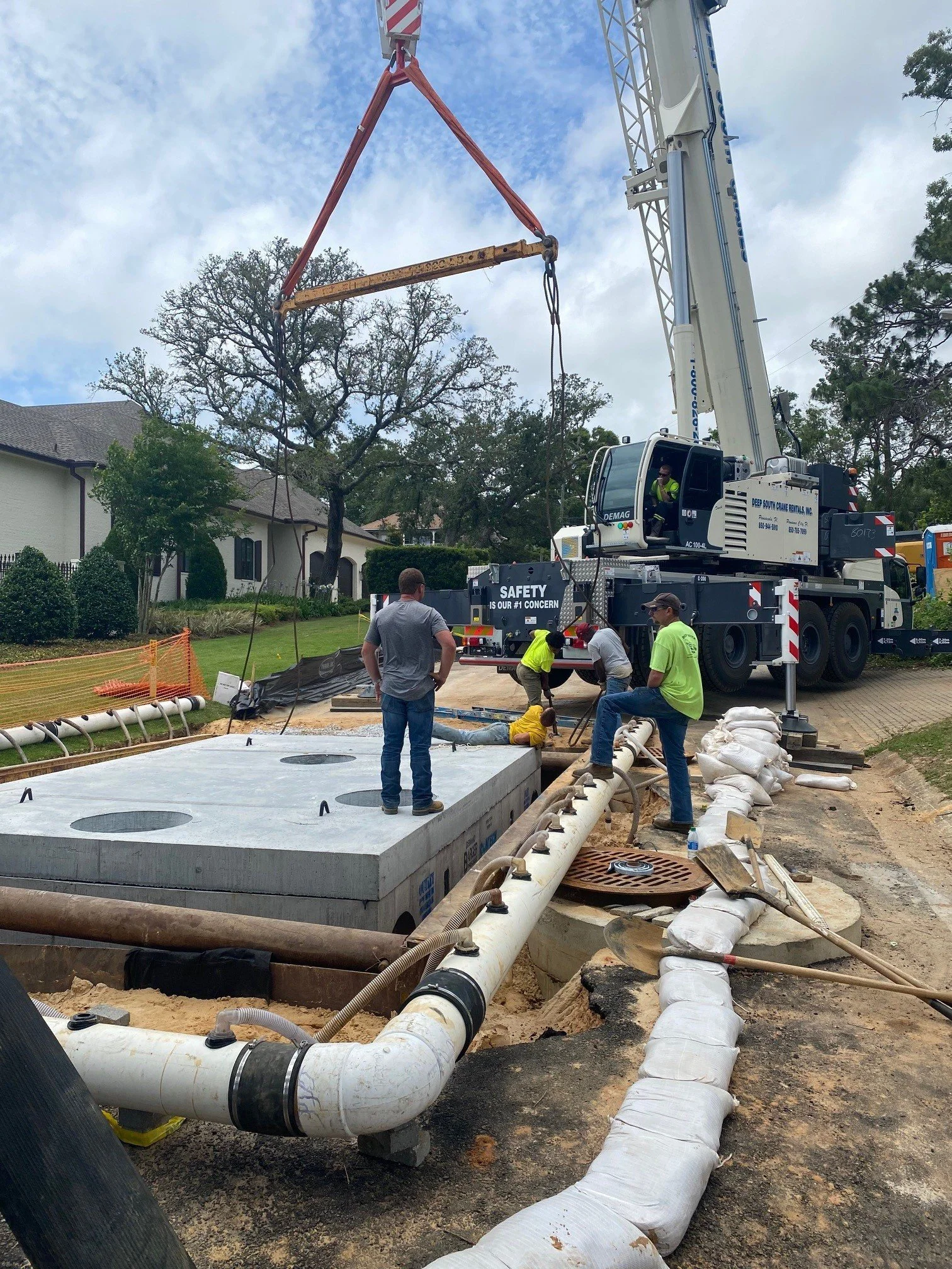 Construction workers and a crane installing or repairing large underground pipes and equipment near a residential area.