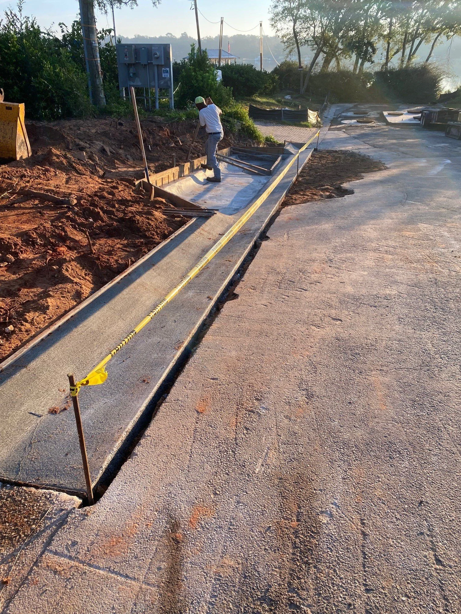 Construction worker laying concrete sidewalk with tools, yellow caution tape, and construction site surroundings