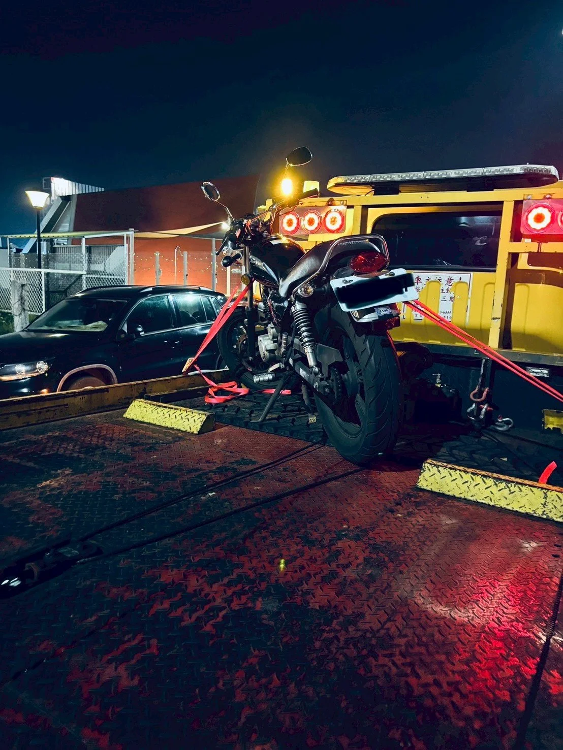 A motorcycle secured with red straps on the back of a flatbed truck at night.