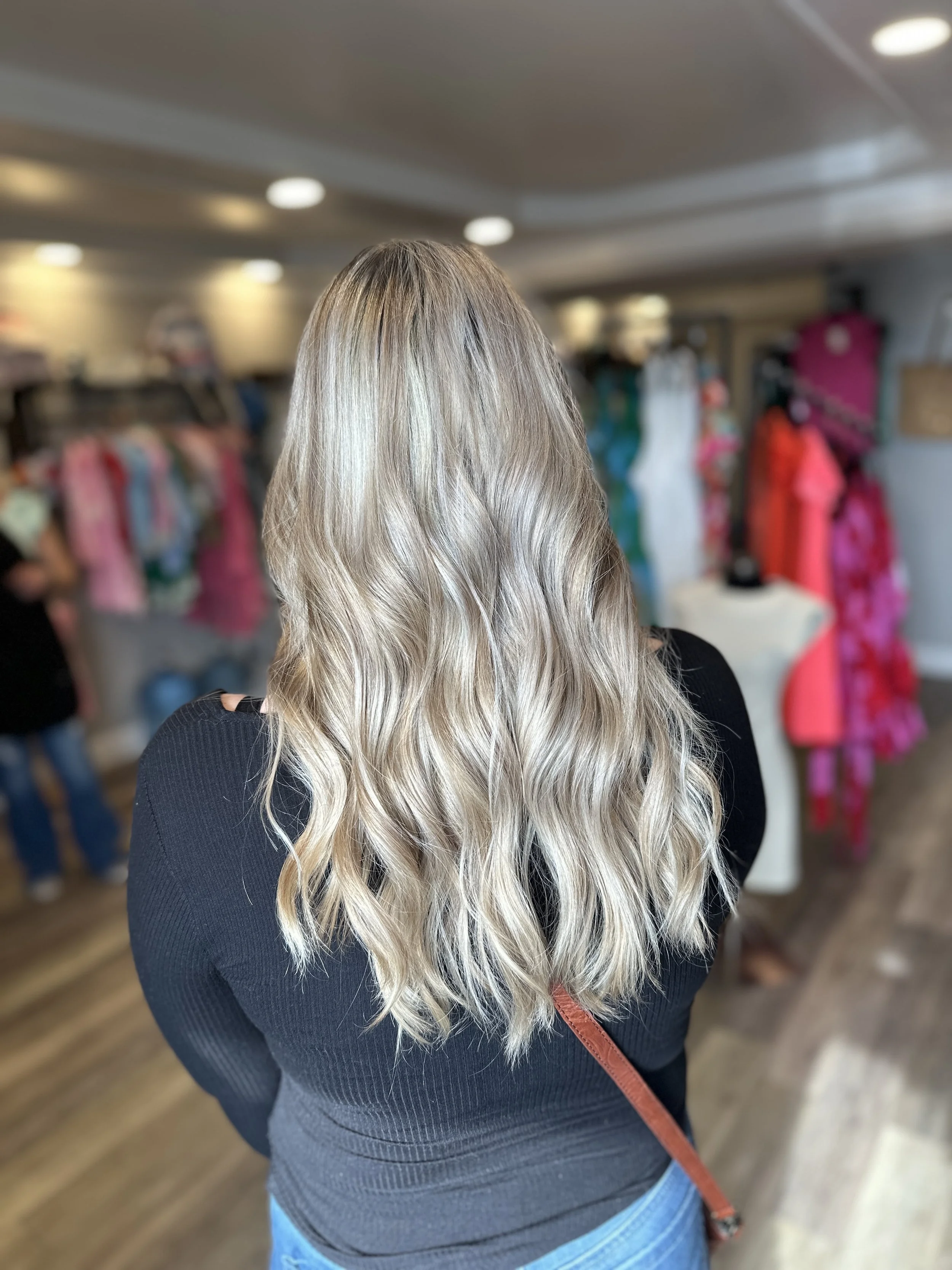 Back view of woman with long, wavy blonde hair in a clothing store.
