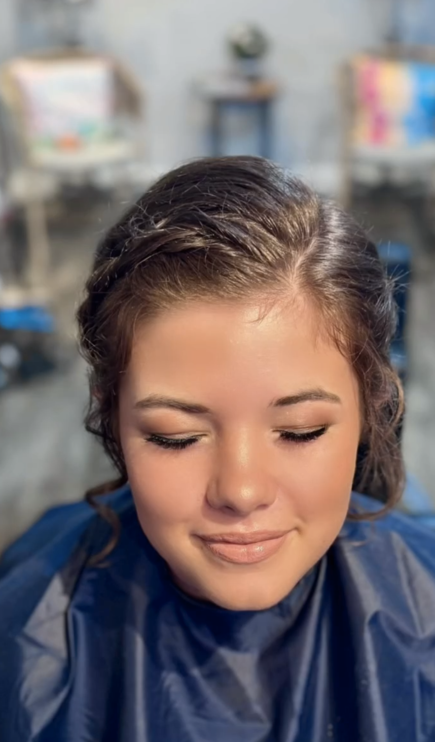 Woman with styled hair sitting in a salon chair, eyes closed, with hairdressing cape on, in a salon setting.