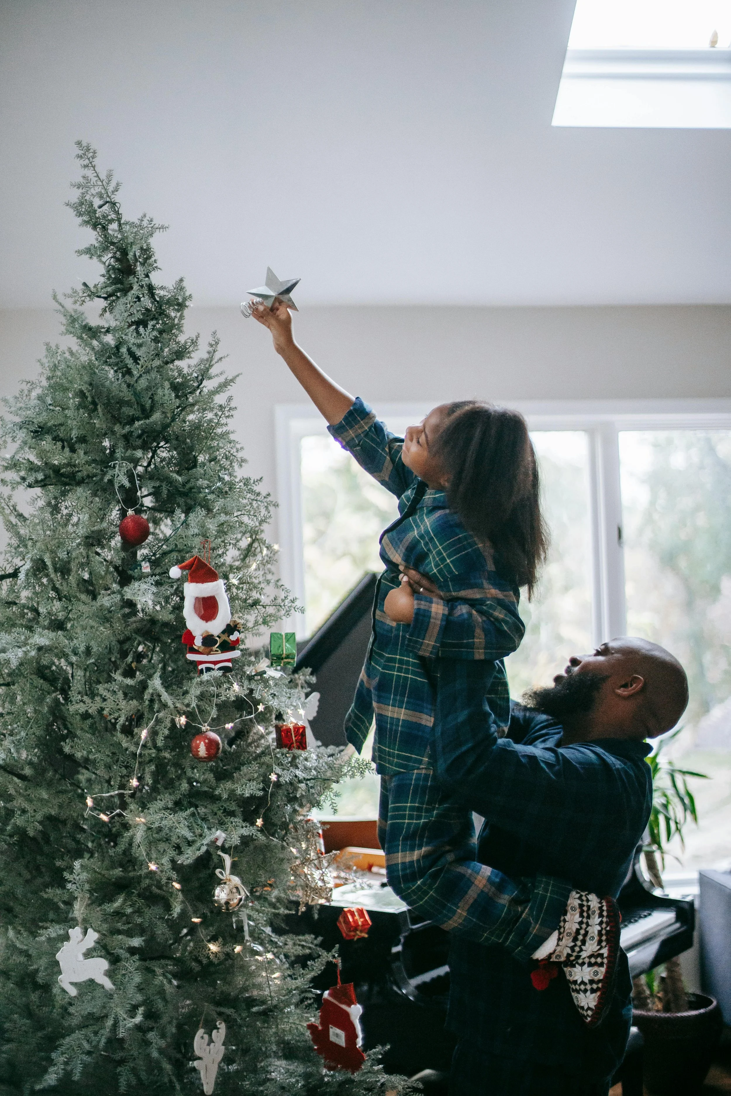 A parent holds their child up to put a star on top of the Christmas tree