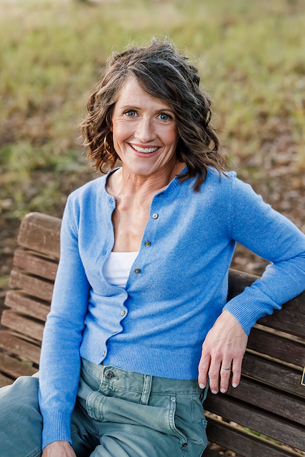 Peggy Raymond, a woman with brown hair wearing a blue cardigan sits on a bench.