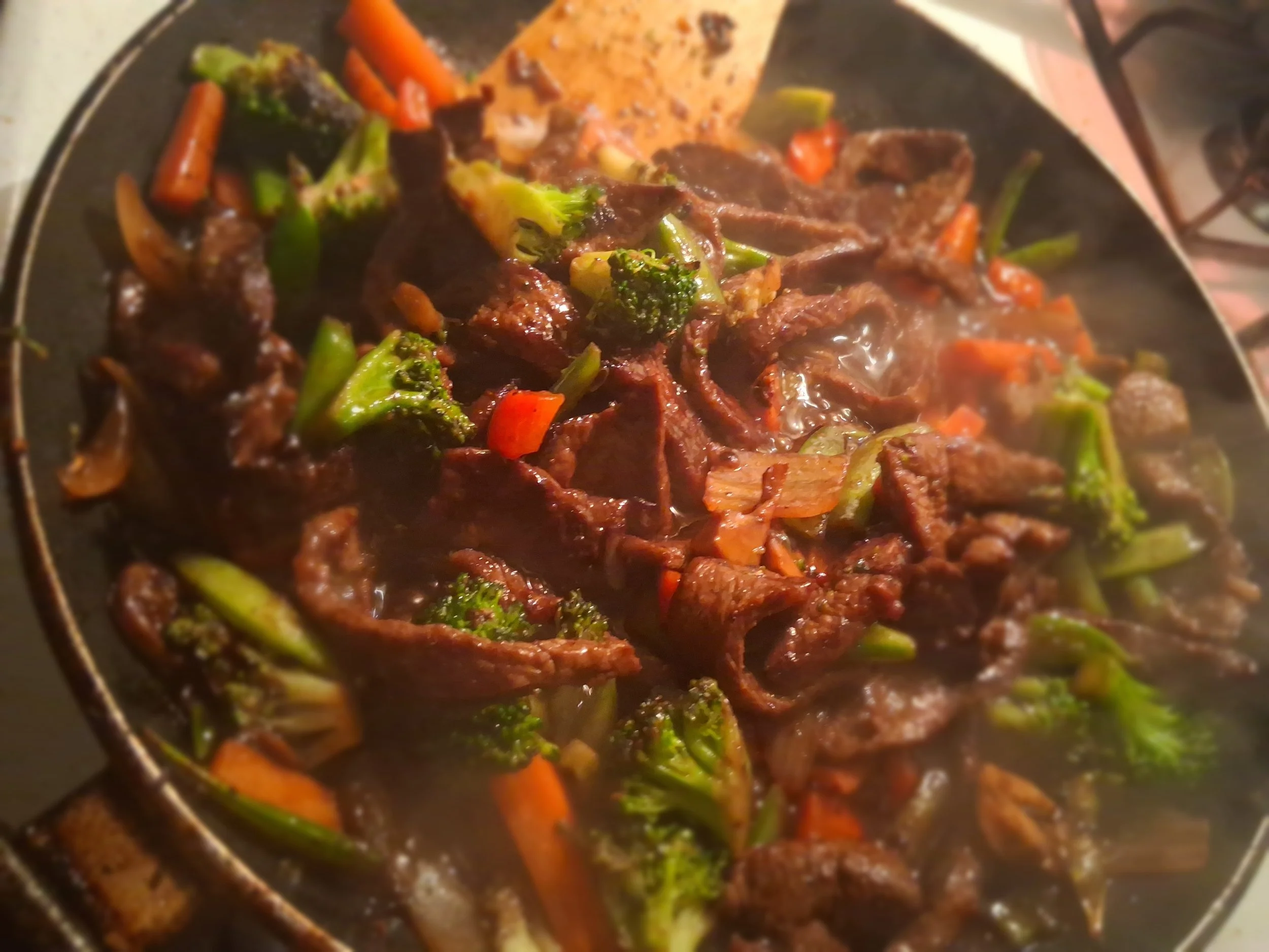 Stir-fried beef with broccoli, carrots, and onions in a black skillet.