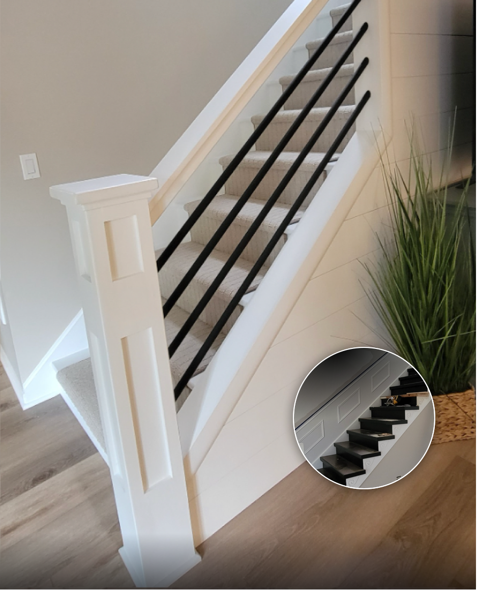 Interior staircase with beige carpet and a white banister with black metal balusters, next to a beige wall with a light switch and a decorative plant.